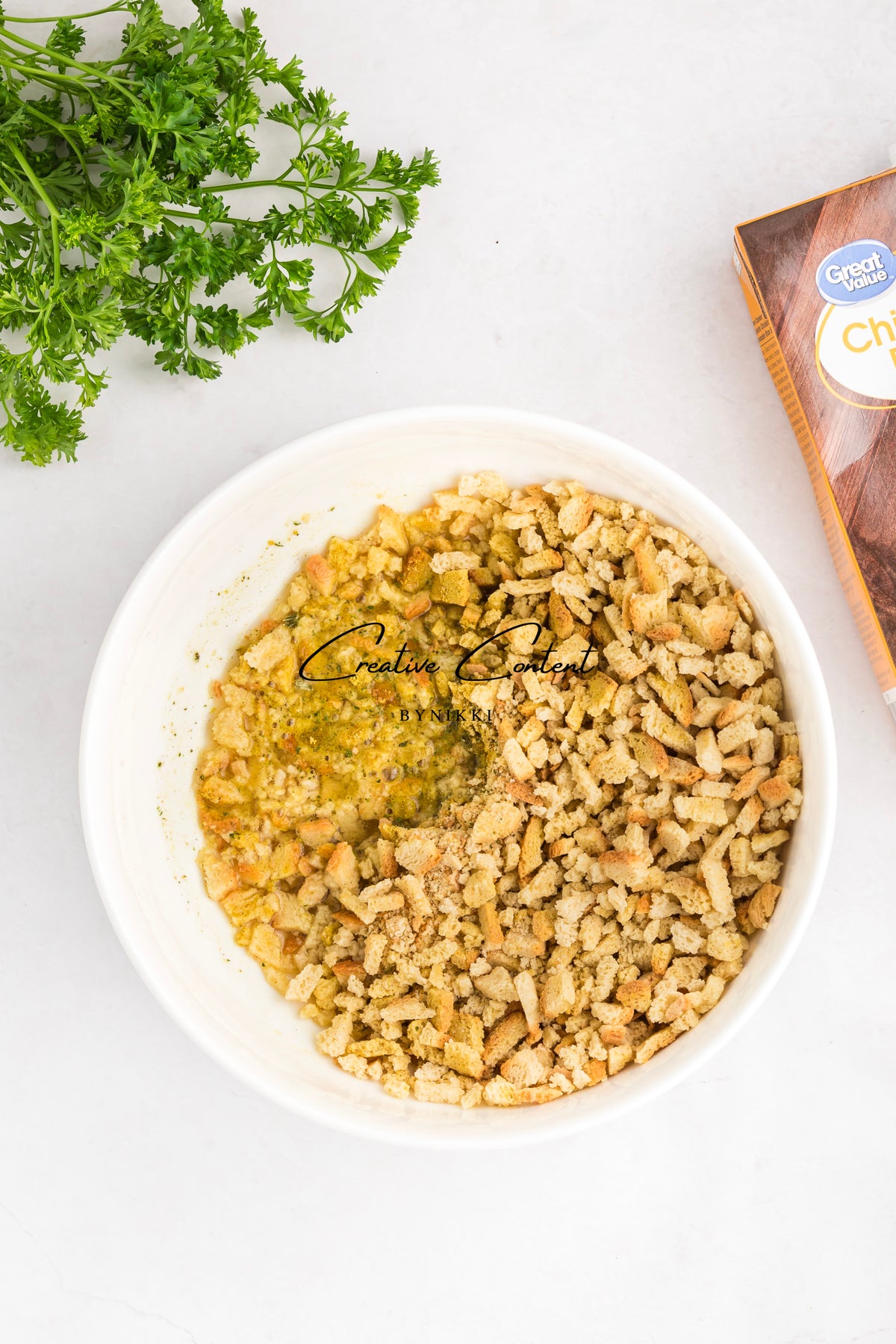 A white bowl containing Church Cookbook Chicken Casserole - Exclusive made with seasoned stuffing cubes, set beside a bunch of fresh parsley and a box of stuffing mix.