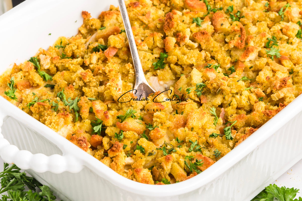 Church Cookbook Chicken Casserole - Exclusive in a white dish filled with golden brown rotisserie chicken and stuffing, topped with fresh green herbs and a serving spoon in the center.