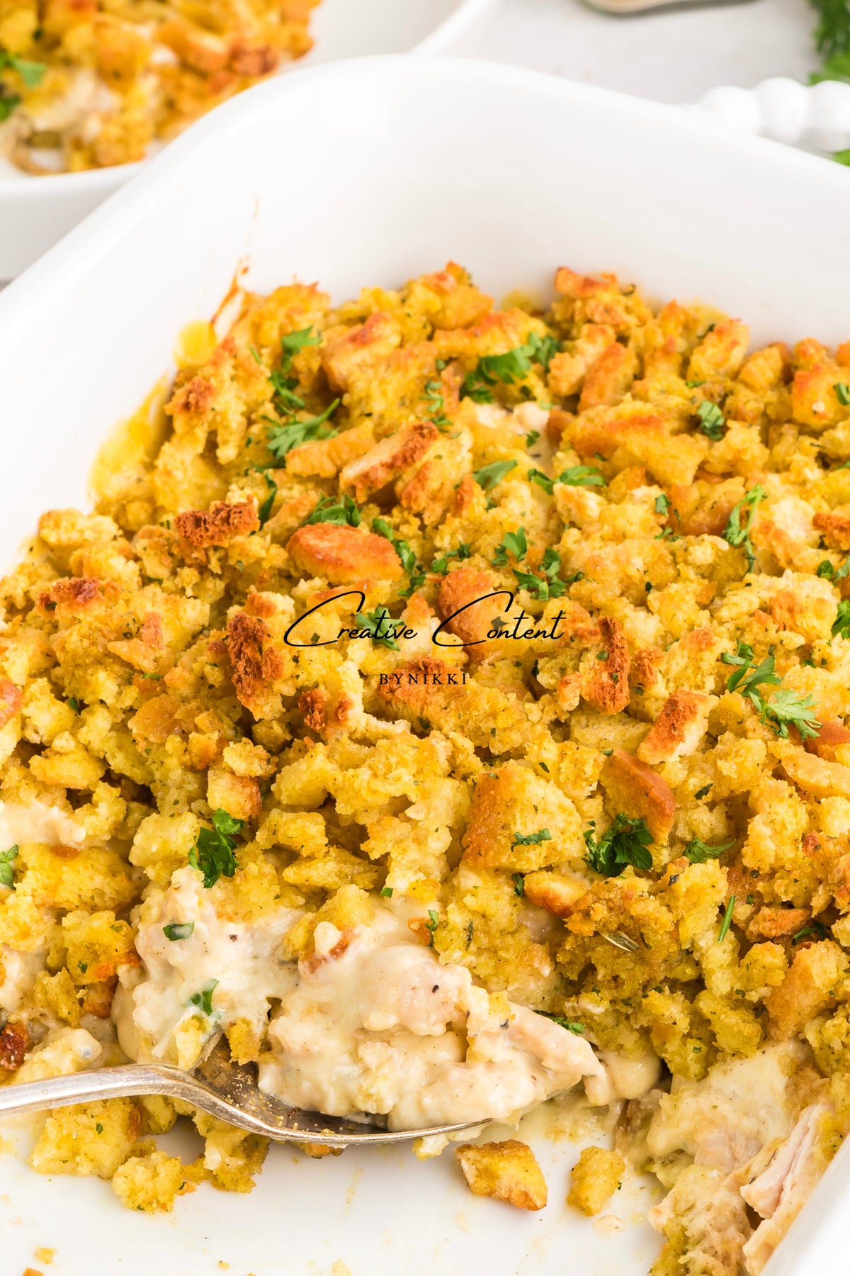 Church Cookbook Chicken Casserole in a creamy rotisserie chicken style, topped with golden brown stuffing and garnished with fresh herbs in a white baking dish with a serving spoon.