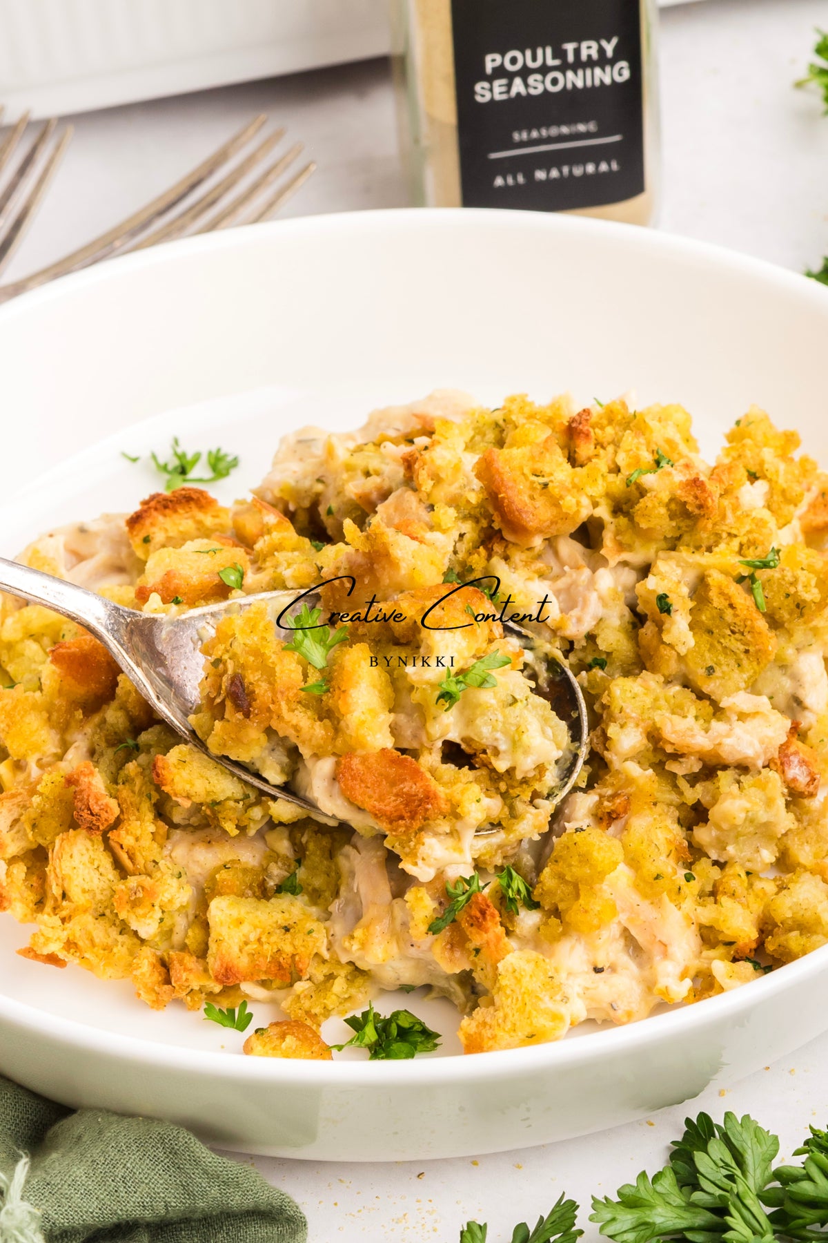 Church cookbook chicken casserole in a white bowl with a spoon and poultry seasoning bottle