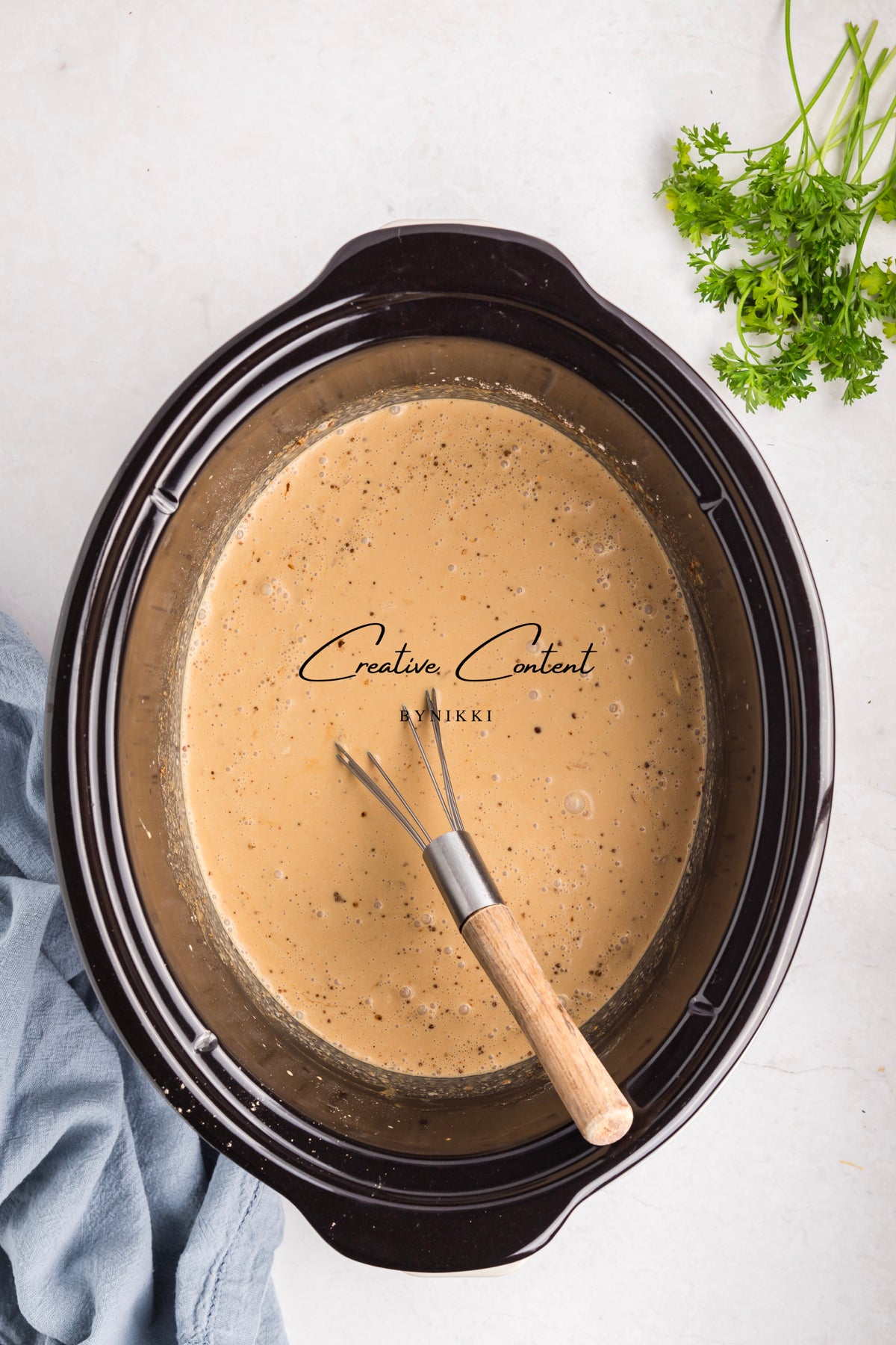 A whisk rests in a slow cooker filled with a creamy brown sauce for Crock Pot Smothered Meatballs and Green Beans - Exclusive.