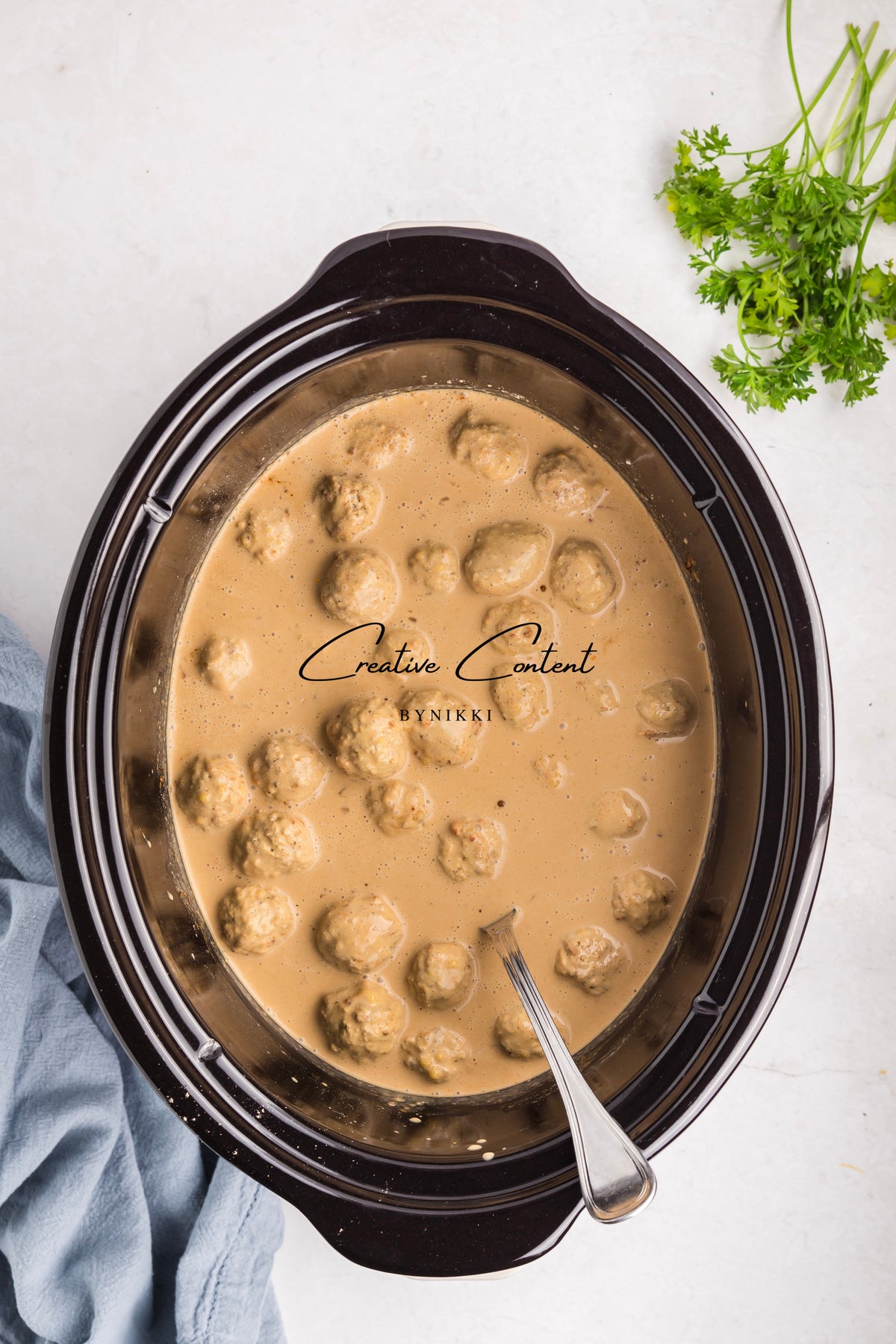 Crock Pot Smothered Meatballs and Green Beans - Exclusive simmering in a creamy brown sauce with a serving spoon and a side of fresh parsley.
