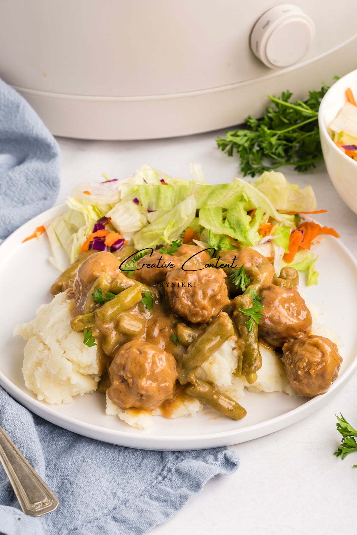 Crock Pot Smothered Meatballs and Green Beans - Exclusive served over mashed potatoes with a side salad on a white plate.
