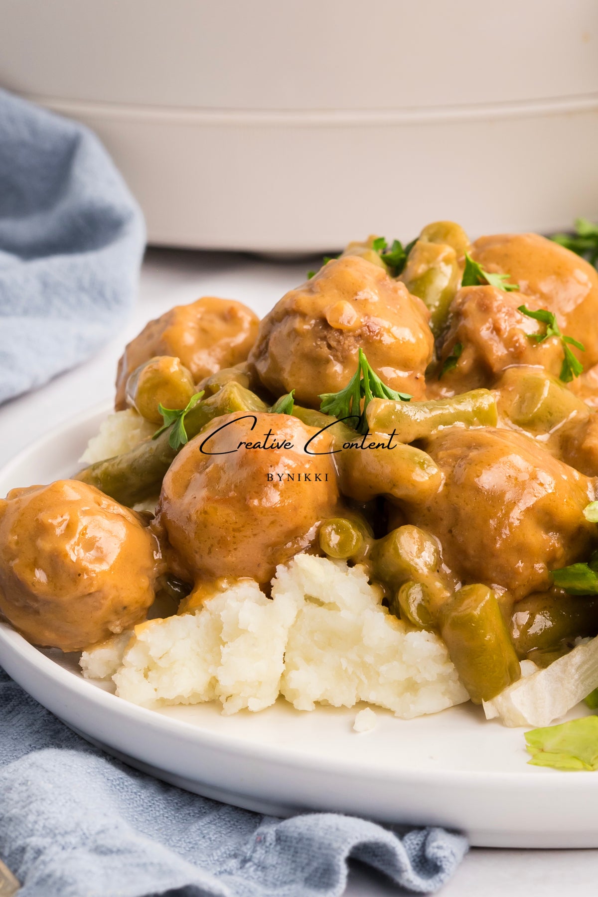 Crock Pot Smothered Meatballs and Green Beans - Exclusive served in a brown gravy over a scoop of mashed potatoes on a white plate.