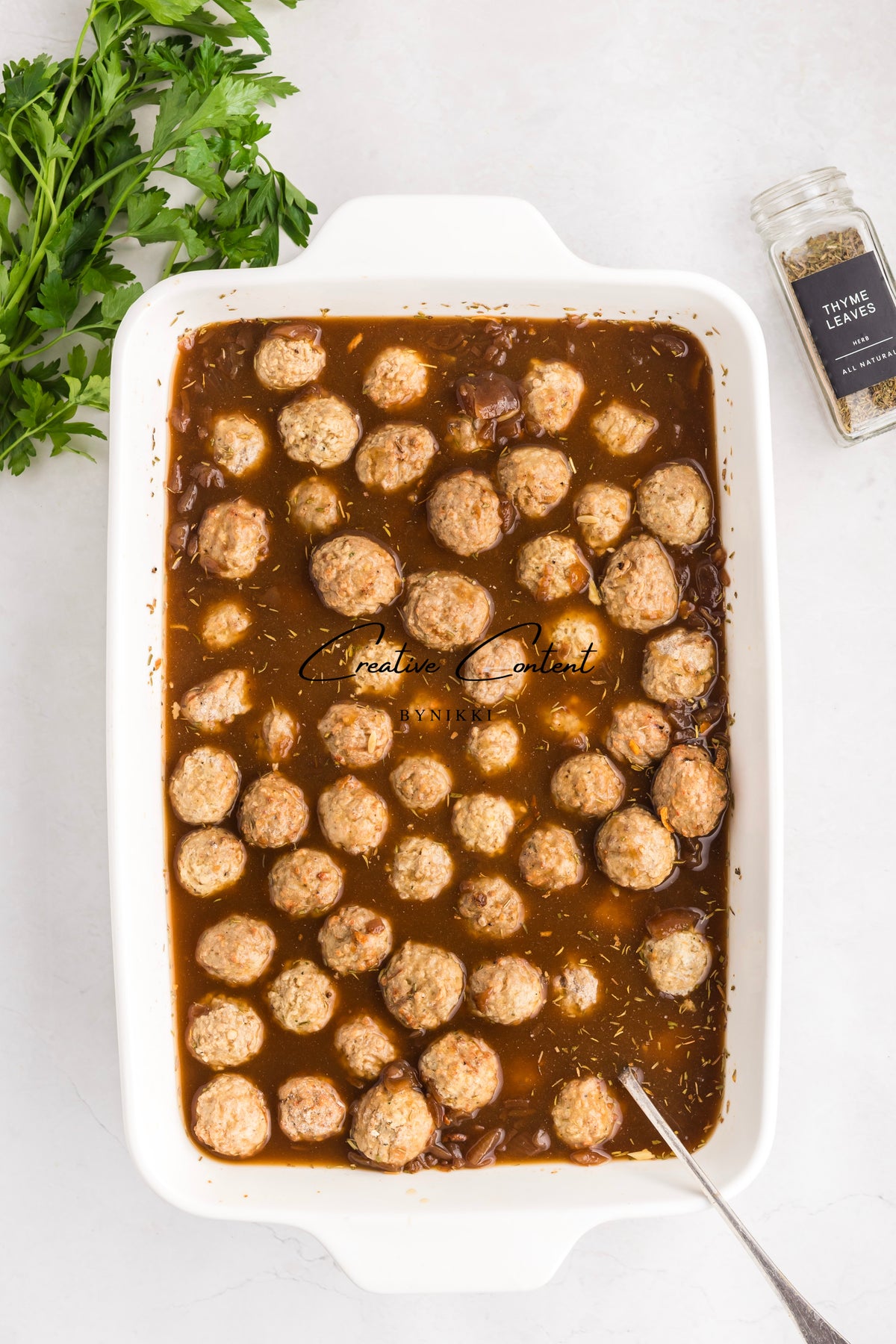 French Onion Meatball Orzo Bake in a white rectangular baking dish with fresh parsley and thyme leaves