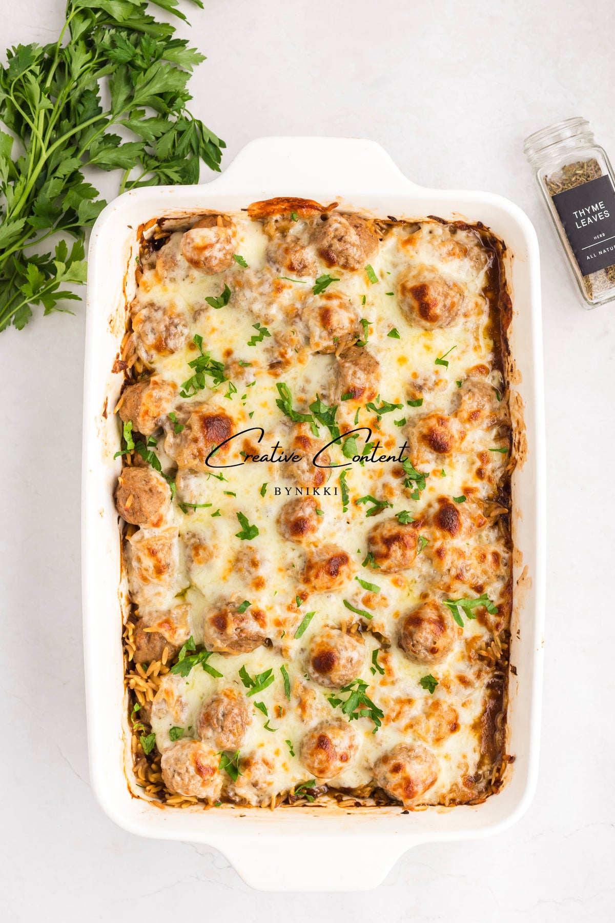 French Onion Meatball Orzo Bake in a white ceramic dish topped with melted cheese and fresh parsley
