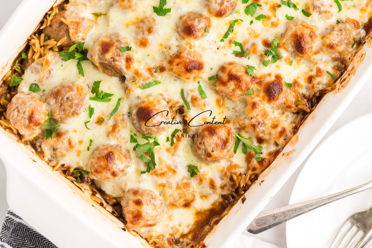 French Onion Meatball Orzo Bake in a baking dish, covered in melted cheese and garnished with chopped parsley.