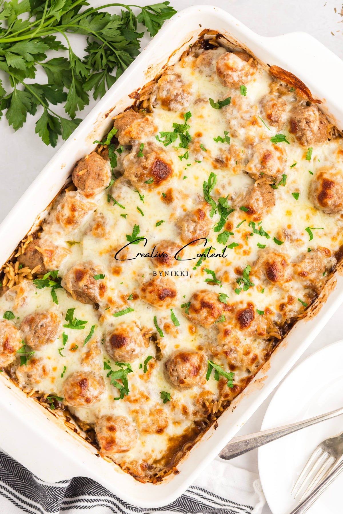 French Onion Meatball Orzo Bake - Exclusive, served in a white casserole dish with melted cheese and fresh parsley.