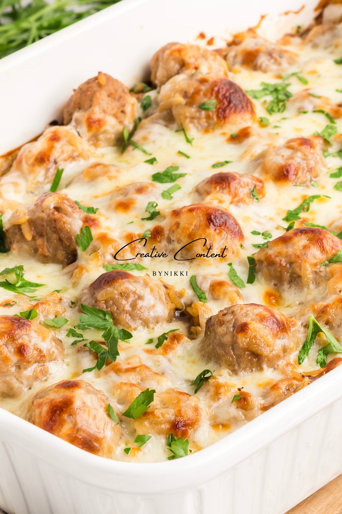 A French Onion Meatball Orzo Bake casserole with melted cheese and fresh parsley.