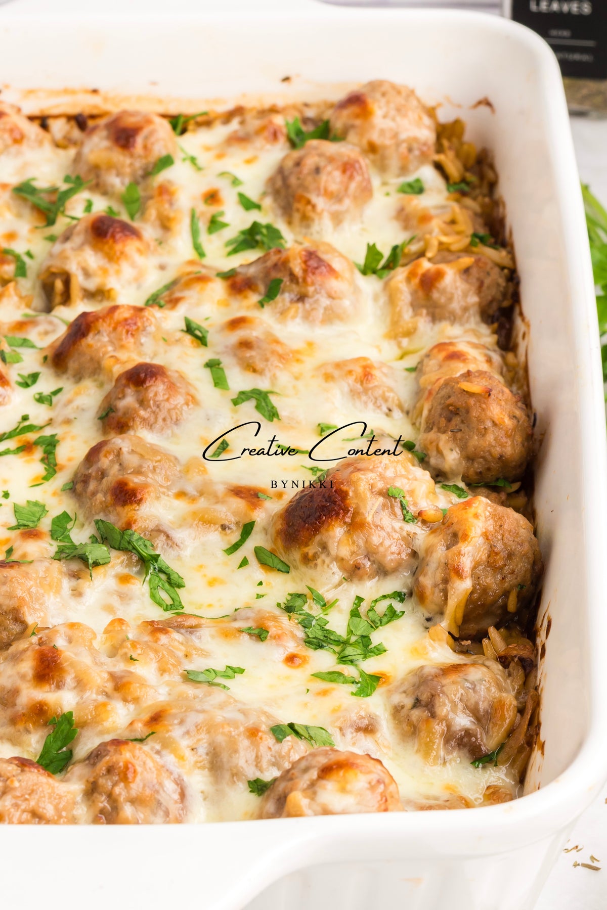 French Onion Meatball Orzo Bake topped with melted cheese and fresh herbs in a white baking dish