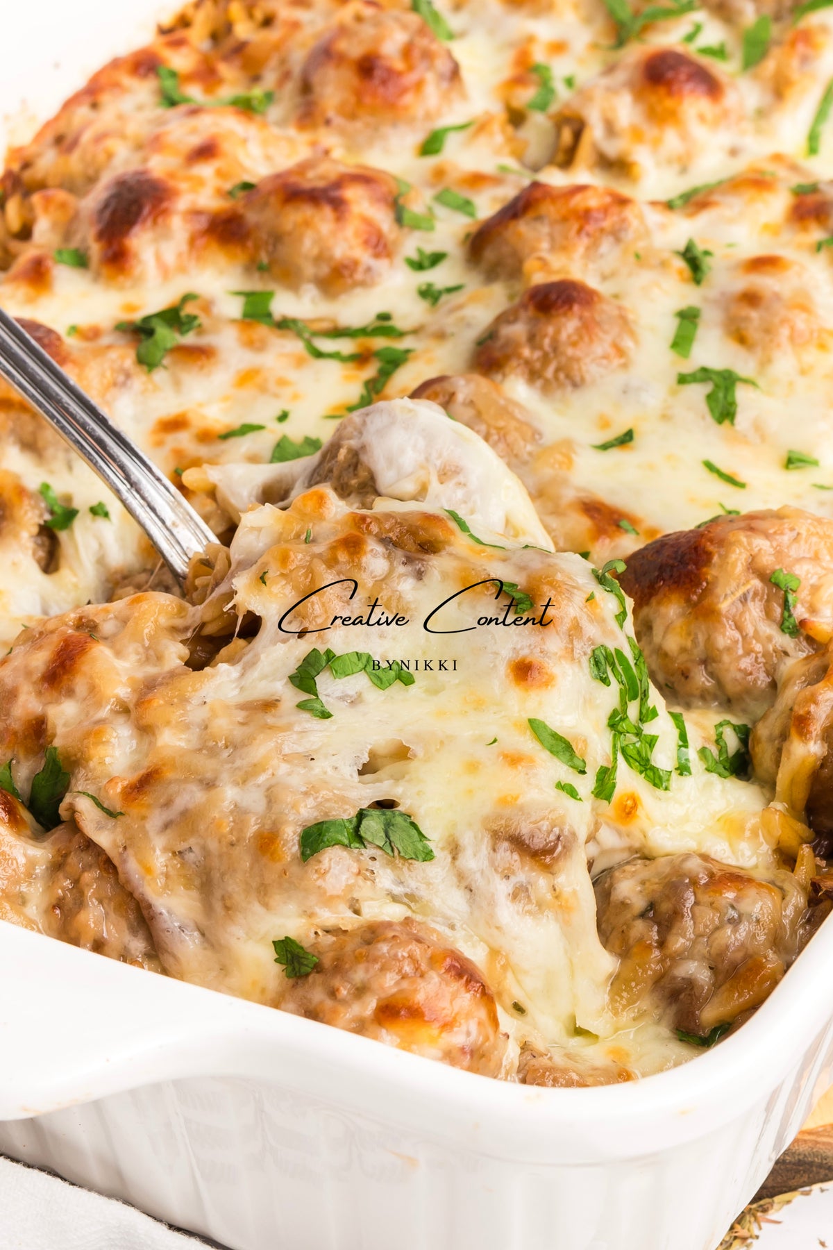 French Onion Meatball Orzo Bake with melted cheese and fresh herbs in a white baking dish