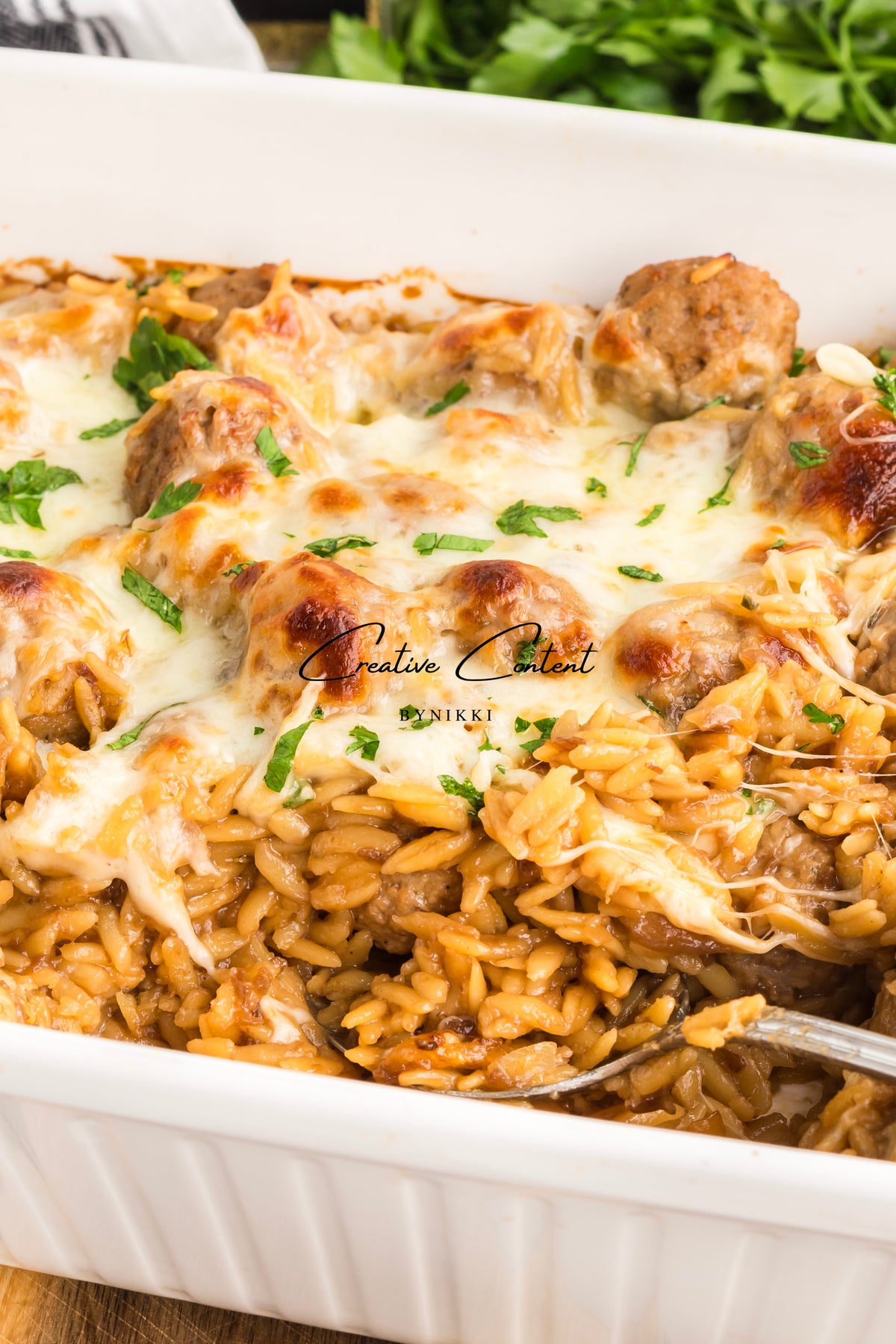 French Onion Meatball Orzo Bake with melted cheese and fresh herbs in a white baking dish