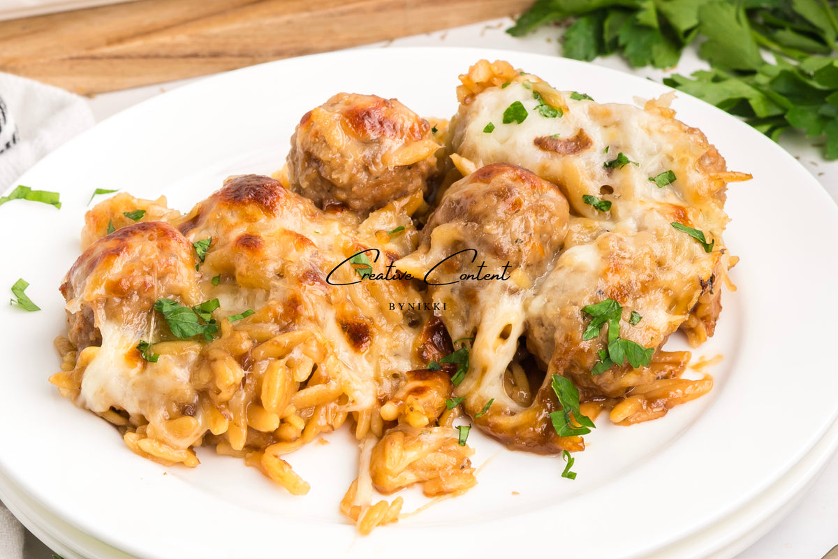 French onion meatball orzo bake topped with melted cheese and fresh herbs on a white plate