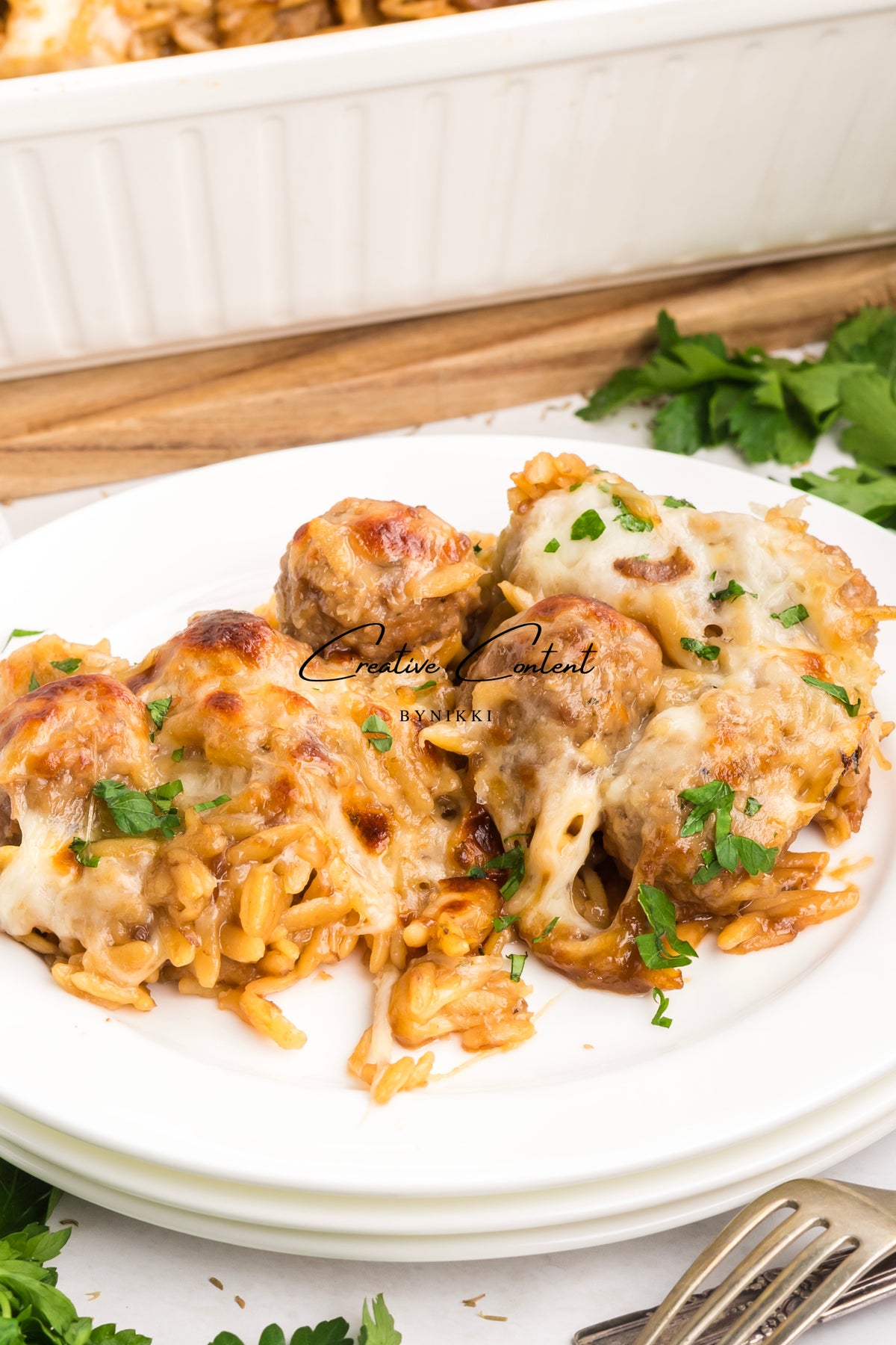 A serving of French Onion Meatball Orzo Bake - Exclusive, topped with melted cheese and fresh herbs on a white plate.
