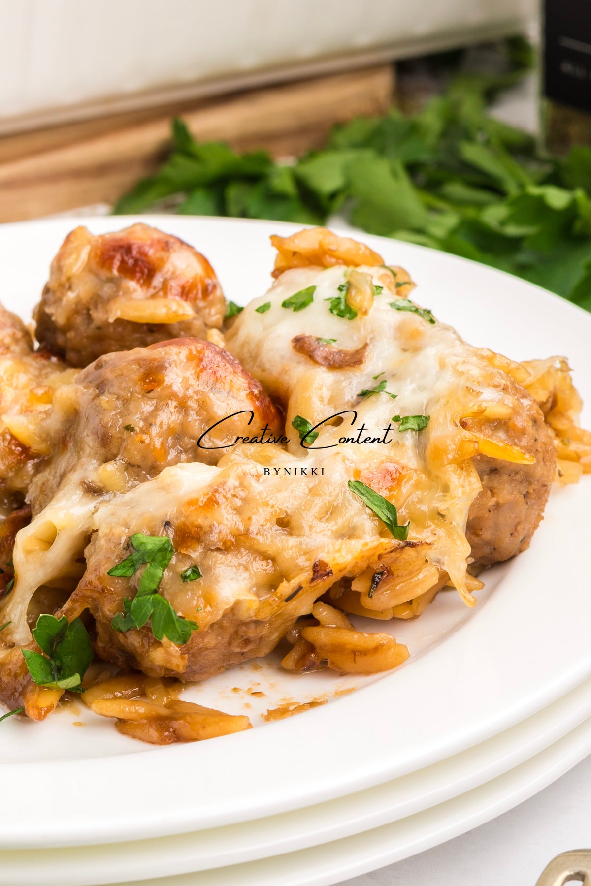French onion meatball orzo bake topped with melted cheese and fresh parsley on a white plate