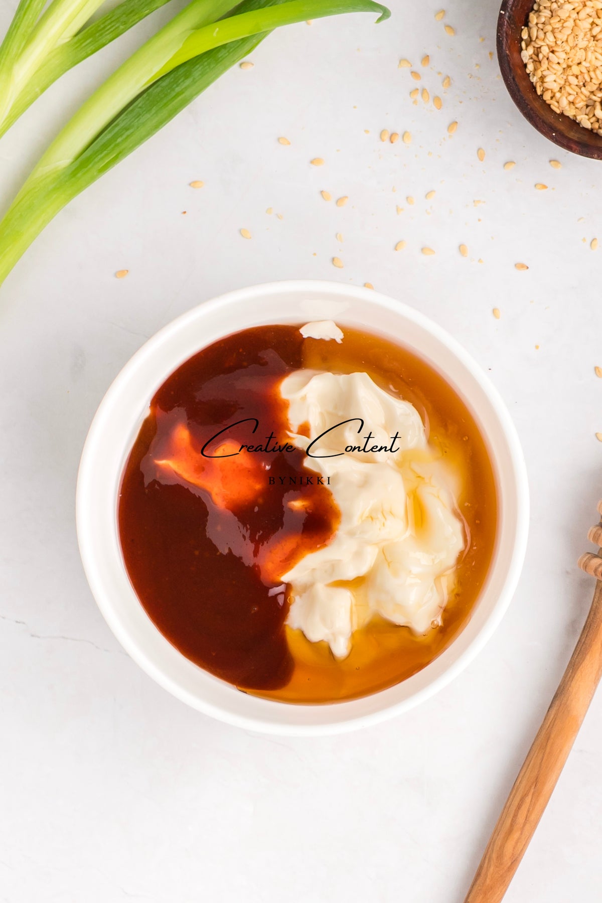 A white bowl containing the dark soy, mayonnaise, and honey base for a Korean Beef Bulgogi - Exclusive sauce, with a green onion and a small dish of sesame seeds nearby for a ground beef rice bowl.