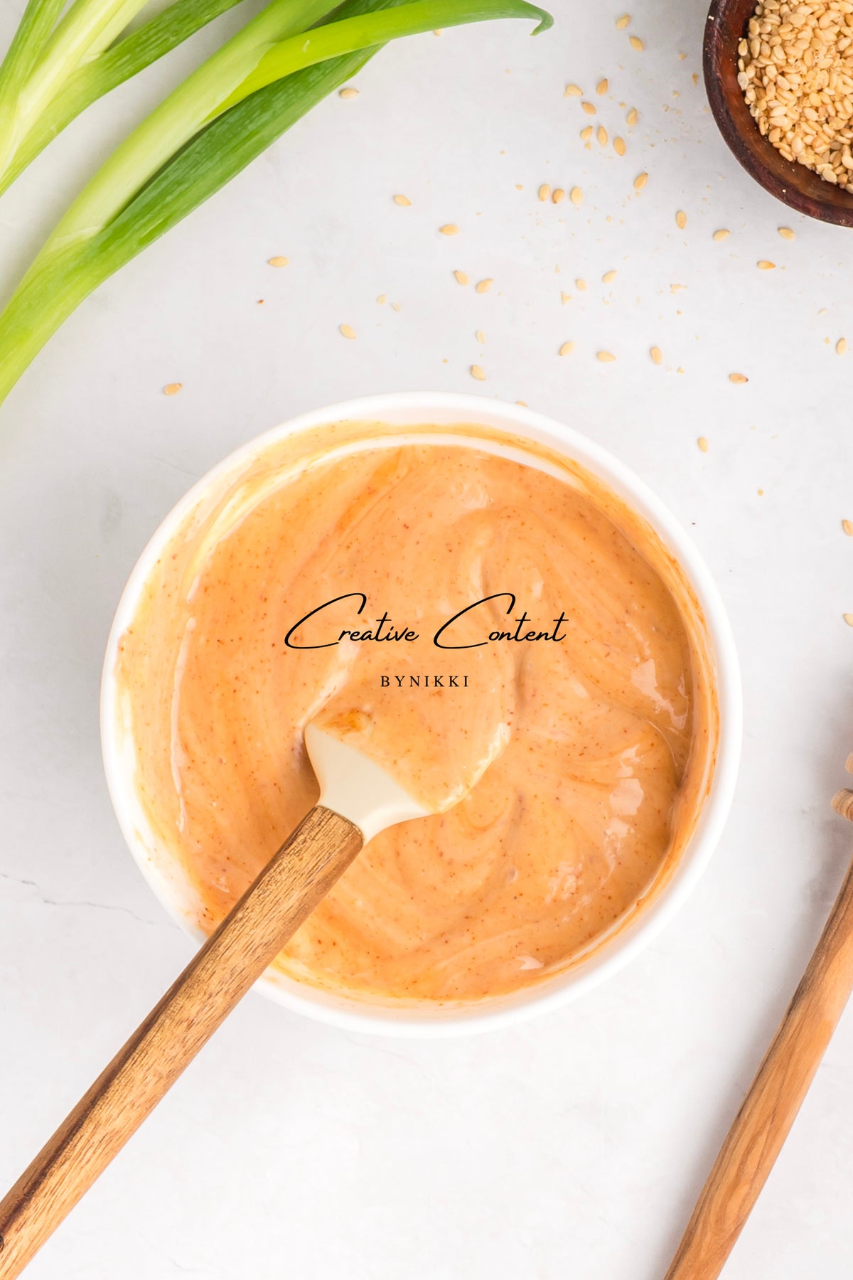 A bowl of creamy gochujang sauce for Korean Beef Bulgogi - Exclusive with a wooden spatula, surrounded by green onions and a small dish of sesame seeds.