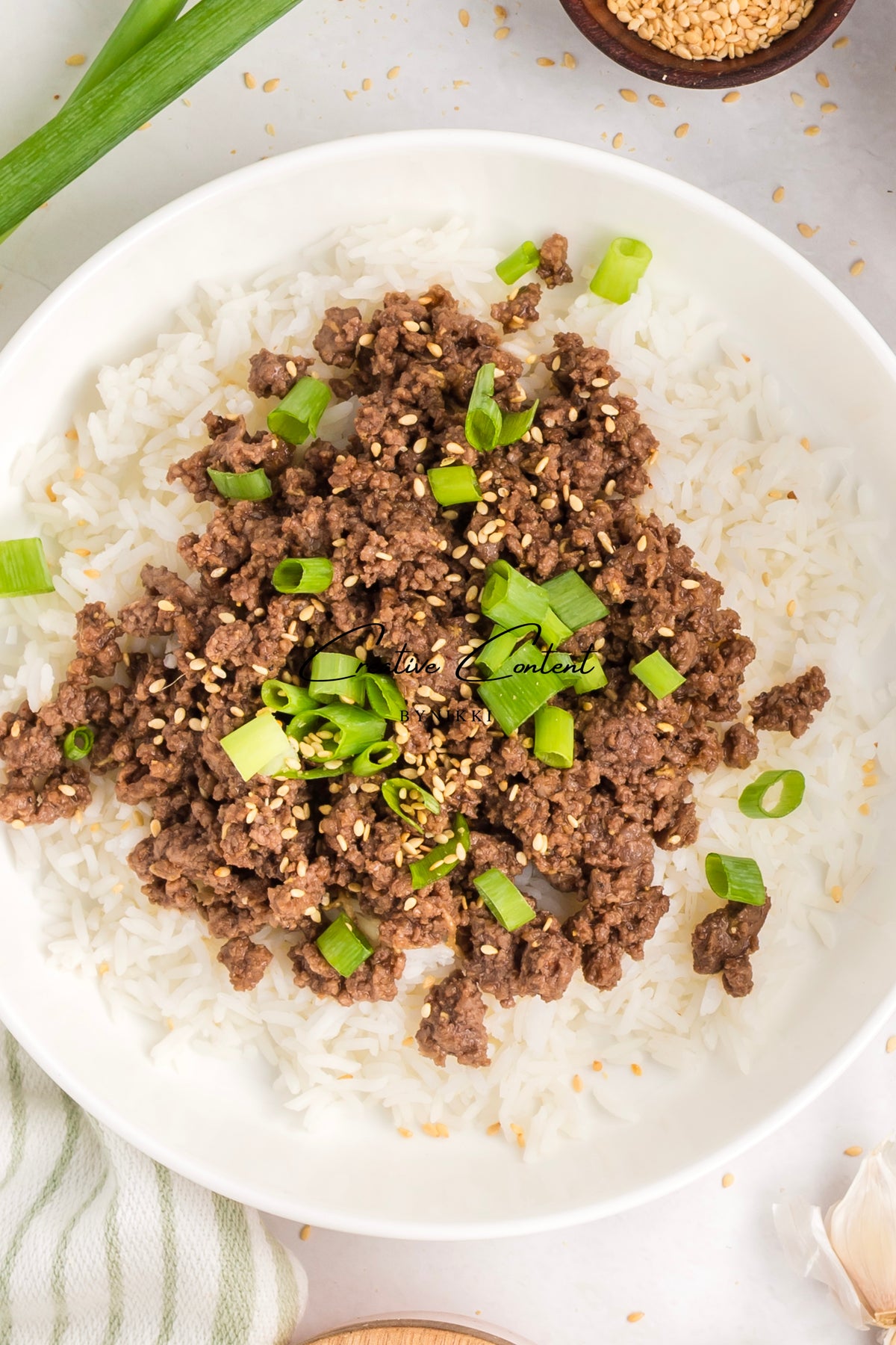 Korean Beef Bulgogi - Exclusive: a bowl of white rice topped with gochujang-sauced ground beef, garnished with sliced green onions and sesame seeds.
