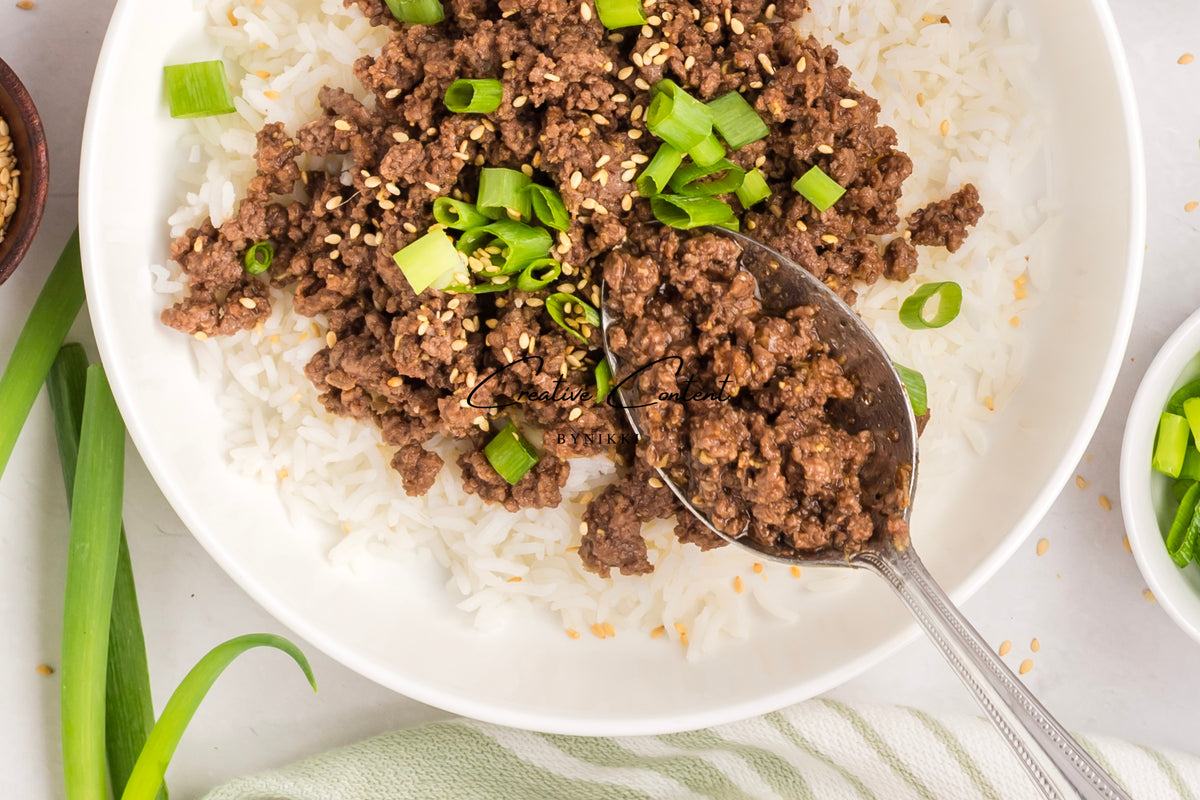 A spoonful of Korean Beef Bulgogi - Exclusive, featuring gochujang-glazed ground beef topped with sesame seeds and chopped green onions, served over a bowl of white rice.