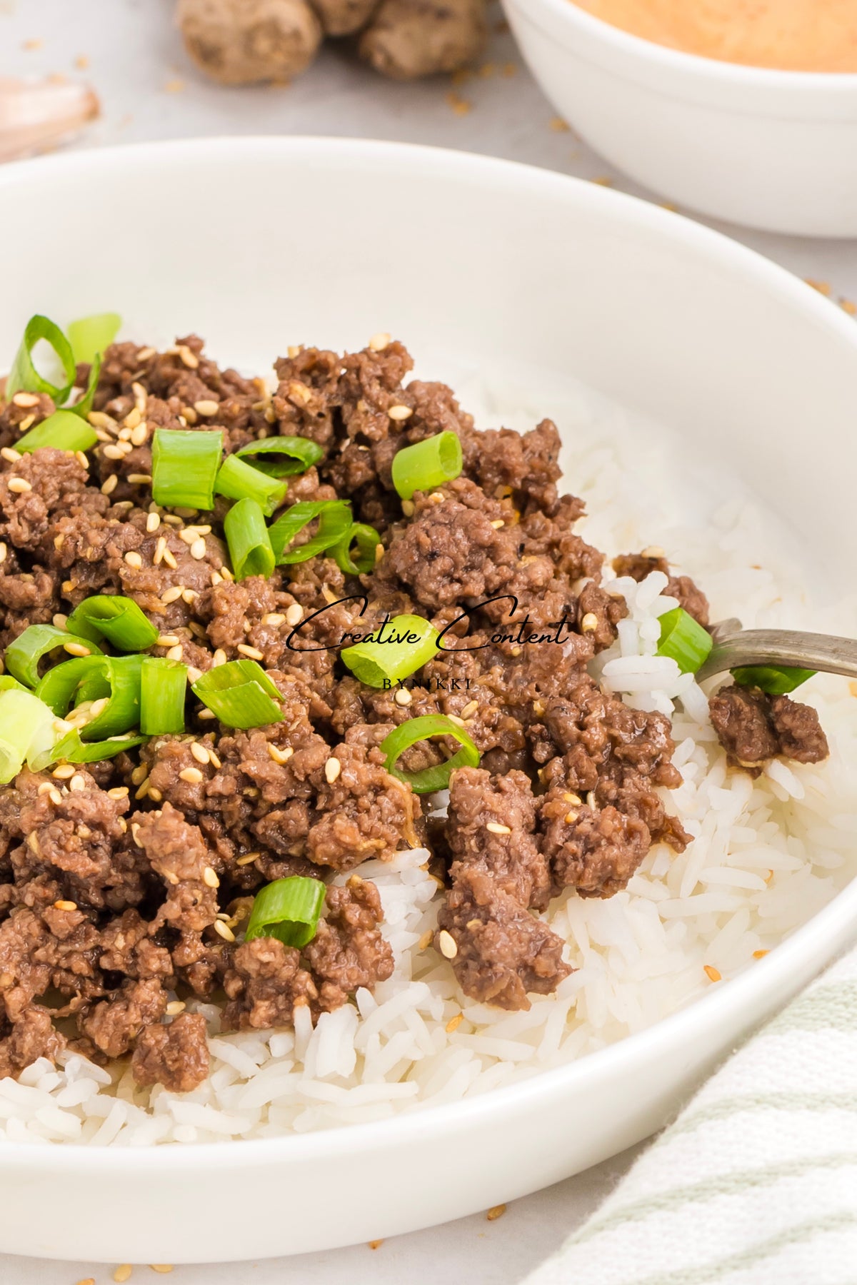 Korean Beef Bulgogi - Exclusive featuring ground beef in a savory gochujang sauce topped with sesame seeds and chopped green onions, served over a bed of white rice in a bowl.