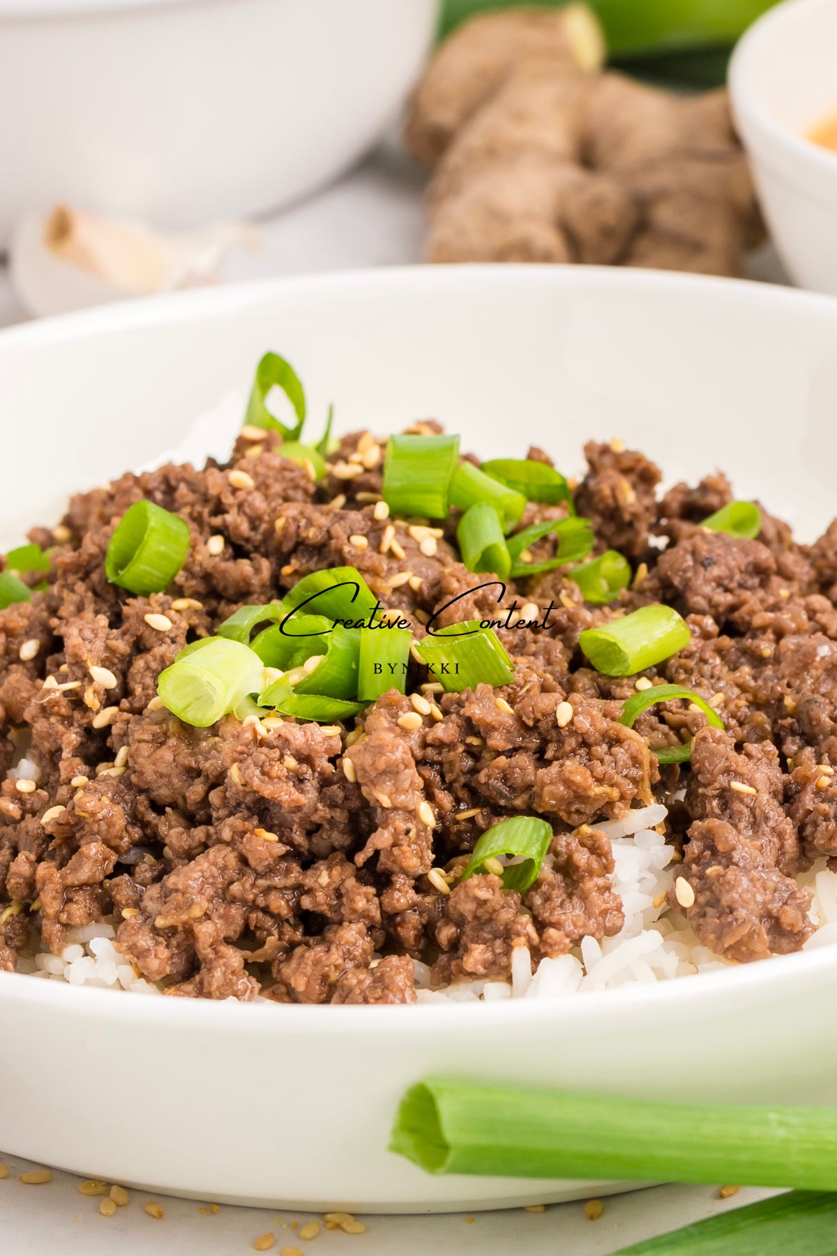 Korean Beef Bulgogi - Exclusive: ground beef in a spicy gochujang sauce topped with sesame seeds and chopped green onions, served over white rice in a white bowl.
