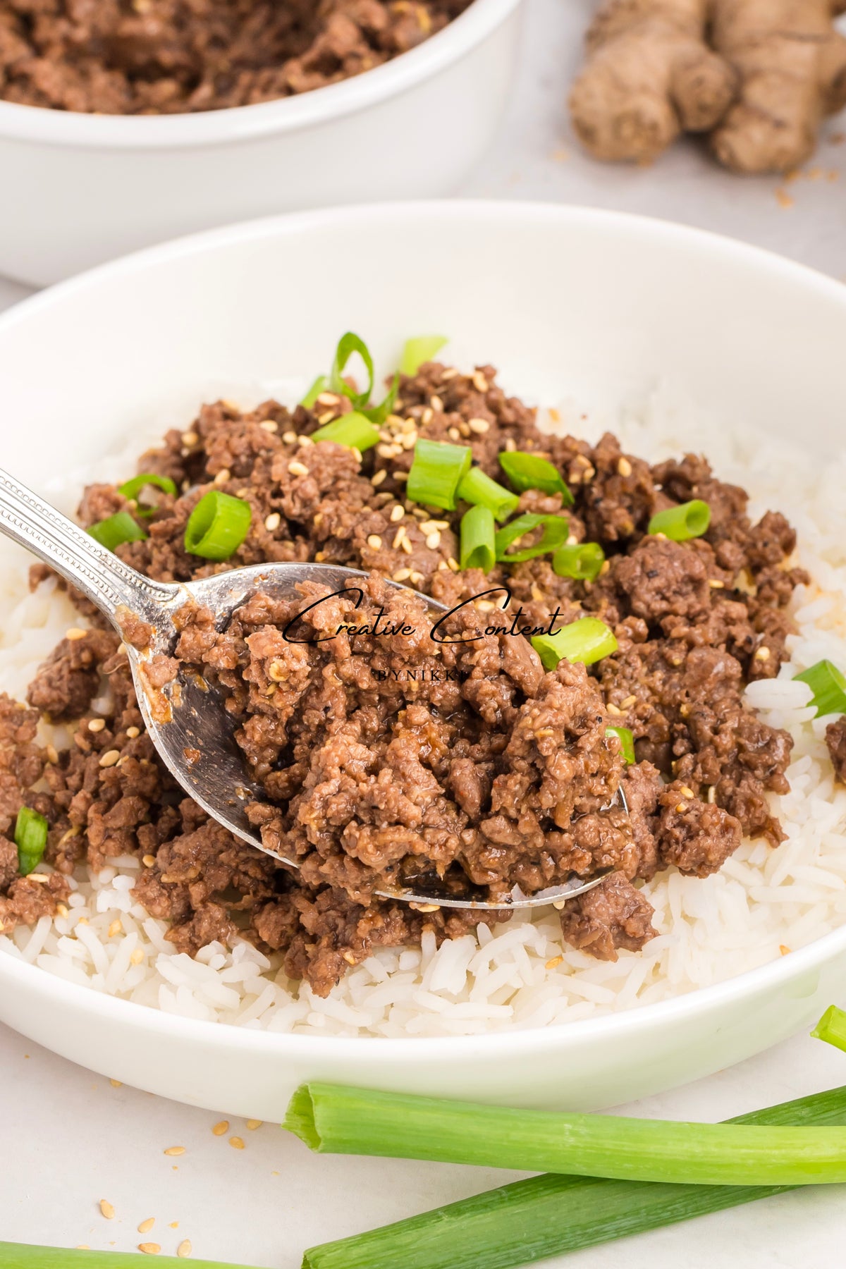 A spoonful of Korean Beef Bulgogi - Exclusive, seasoned with gochujang, green onions, and sesame seeds, held over a bowl of white rice.