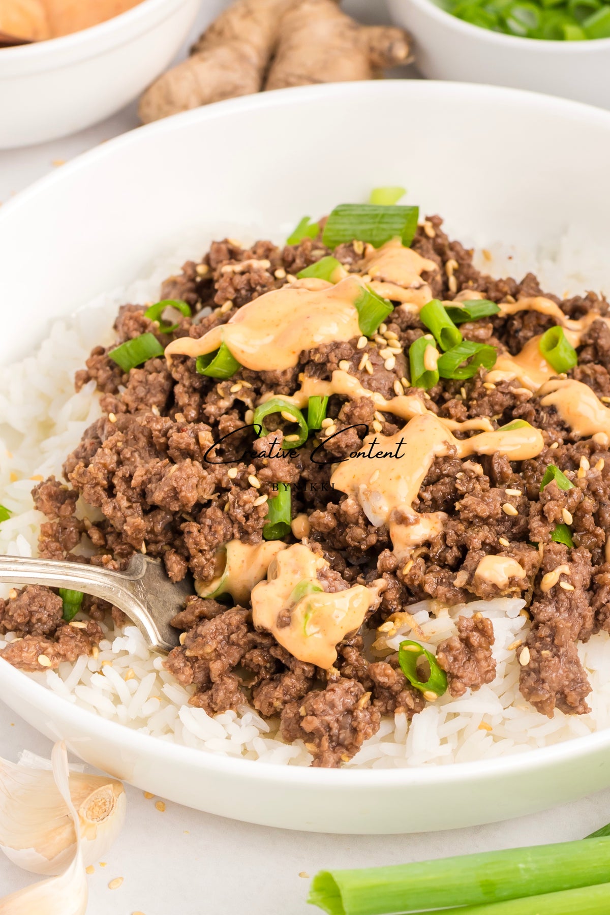 Korean Beef Bulgogi - Exclusive featuring ground beef topped with gochujang sauce, sesame seeds, and sliced green onions, served over a bowl of white rice.