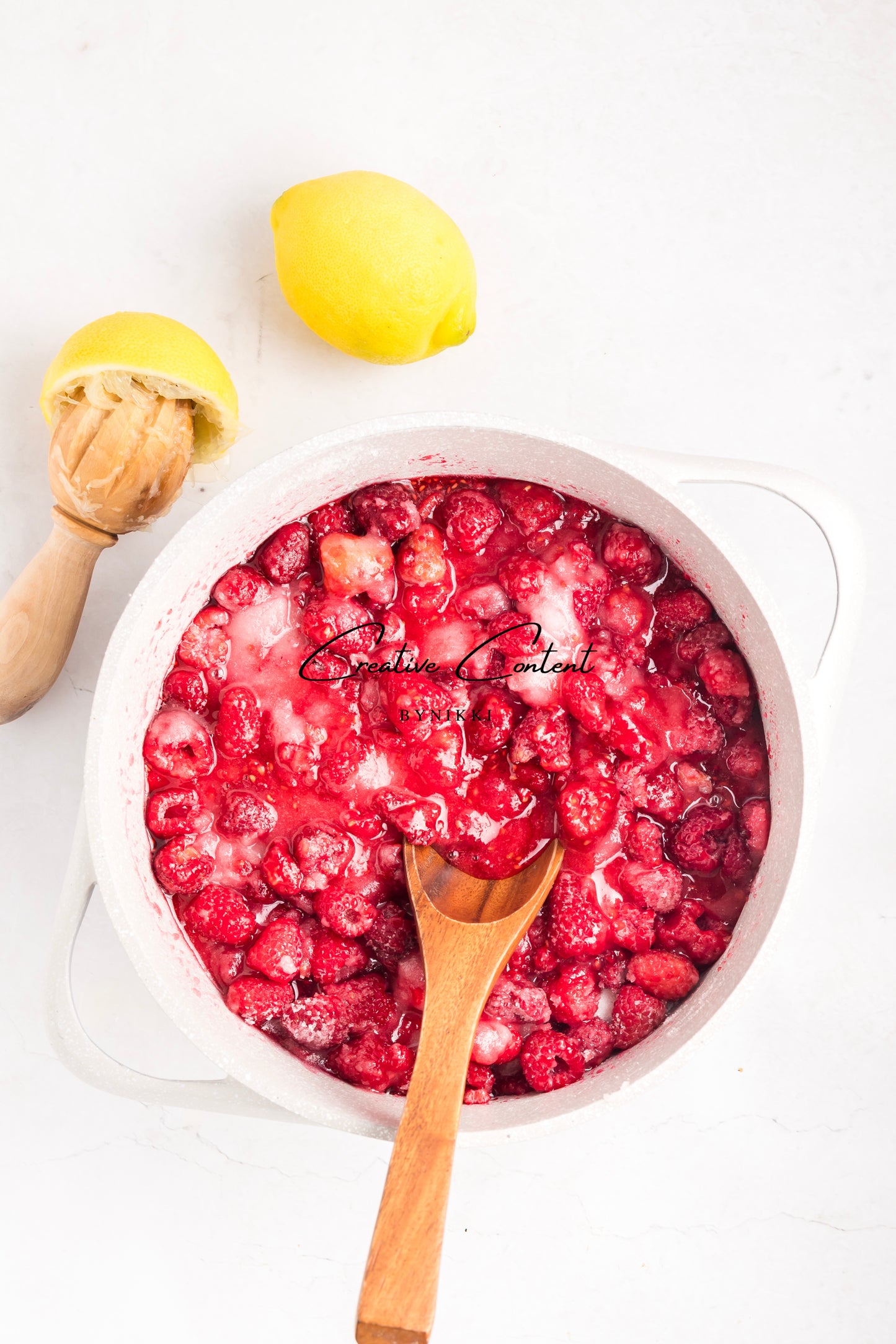 Rasberry sauce in a white pot with a wooden spoon on a white background