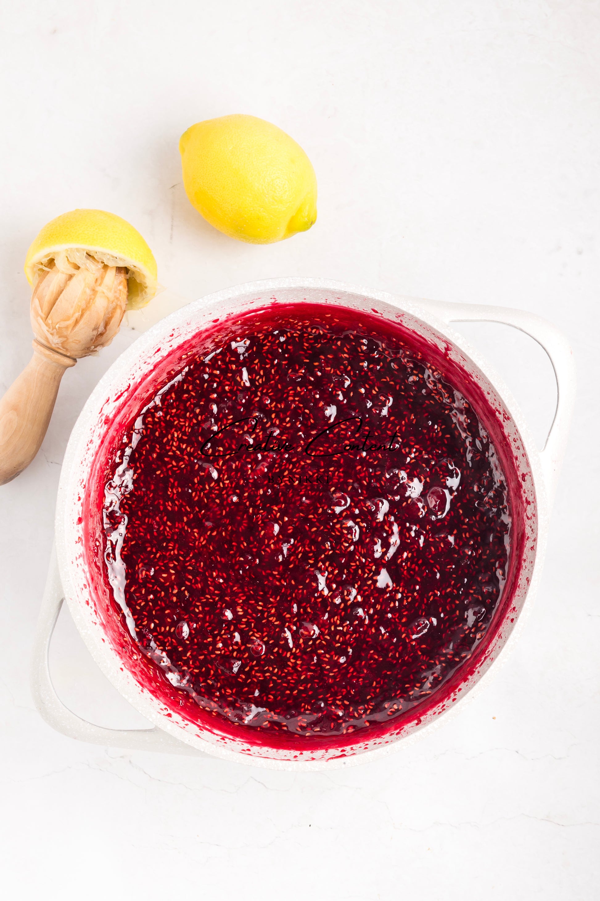 Red berry sauce in a glass container with lemons on a white background