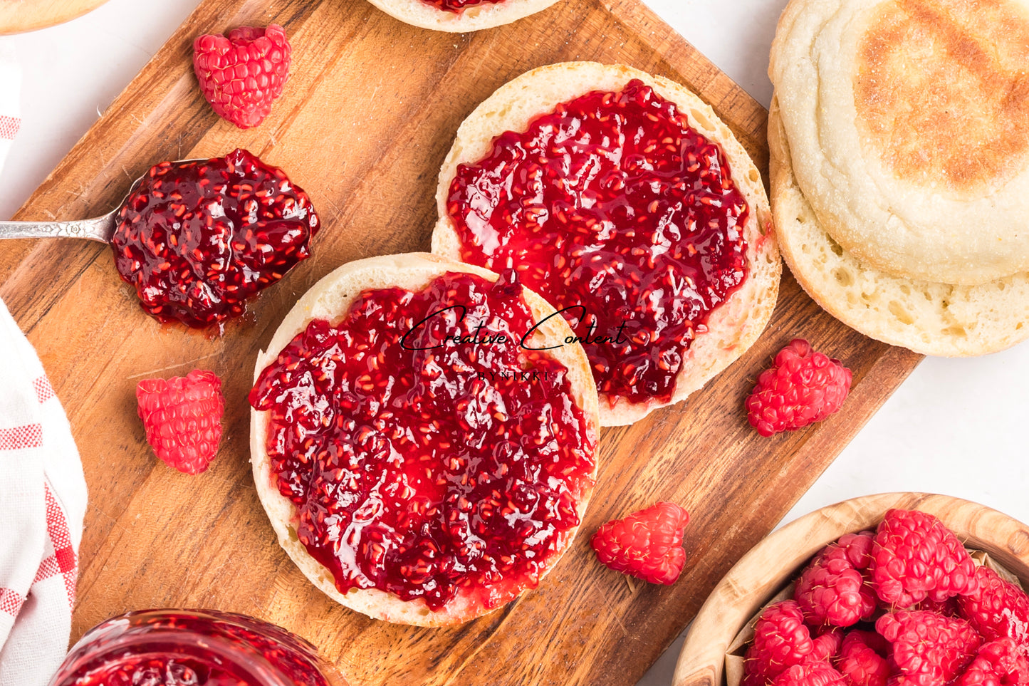 English muffins with raspberry jam on a wooden cutting board with fresh raspberries.