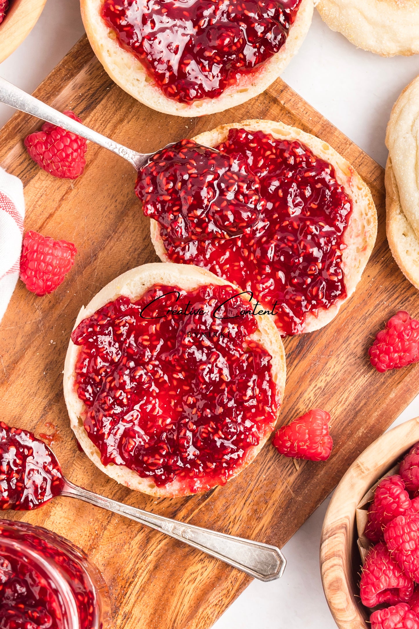 Biscuits topped with raspberry jam on a wooden board with fresh raspberries.