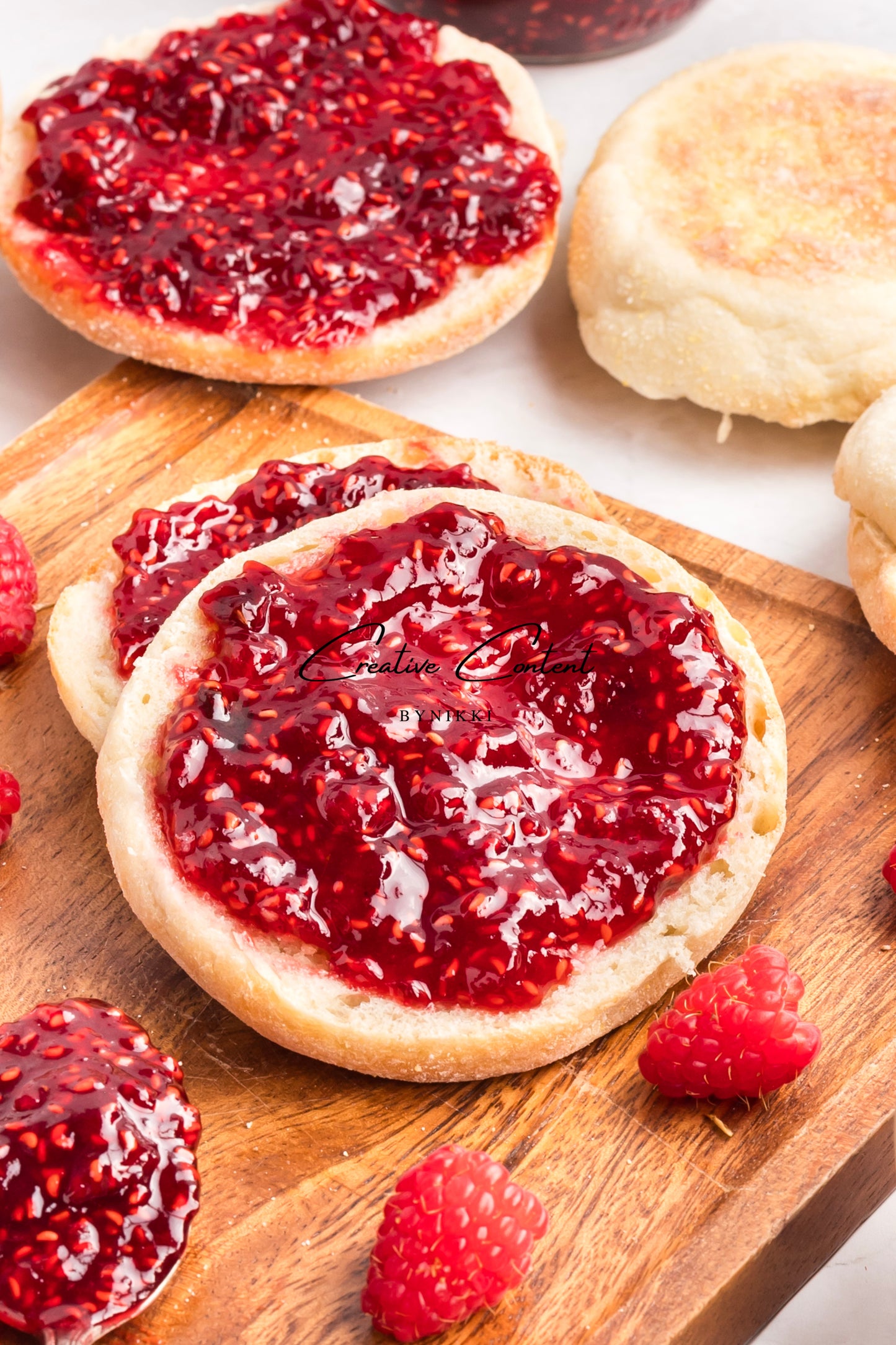 English muffins with raspberry jam on a wooden board with raspberries around.