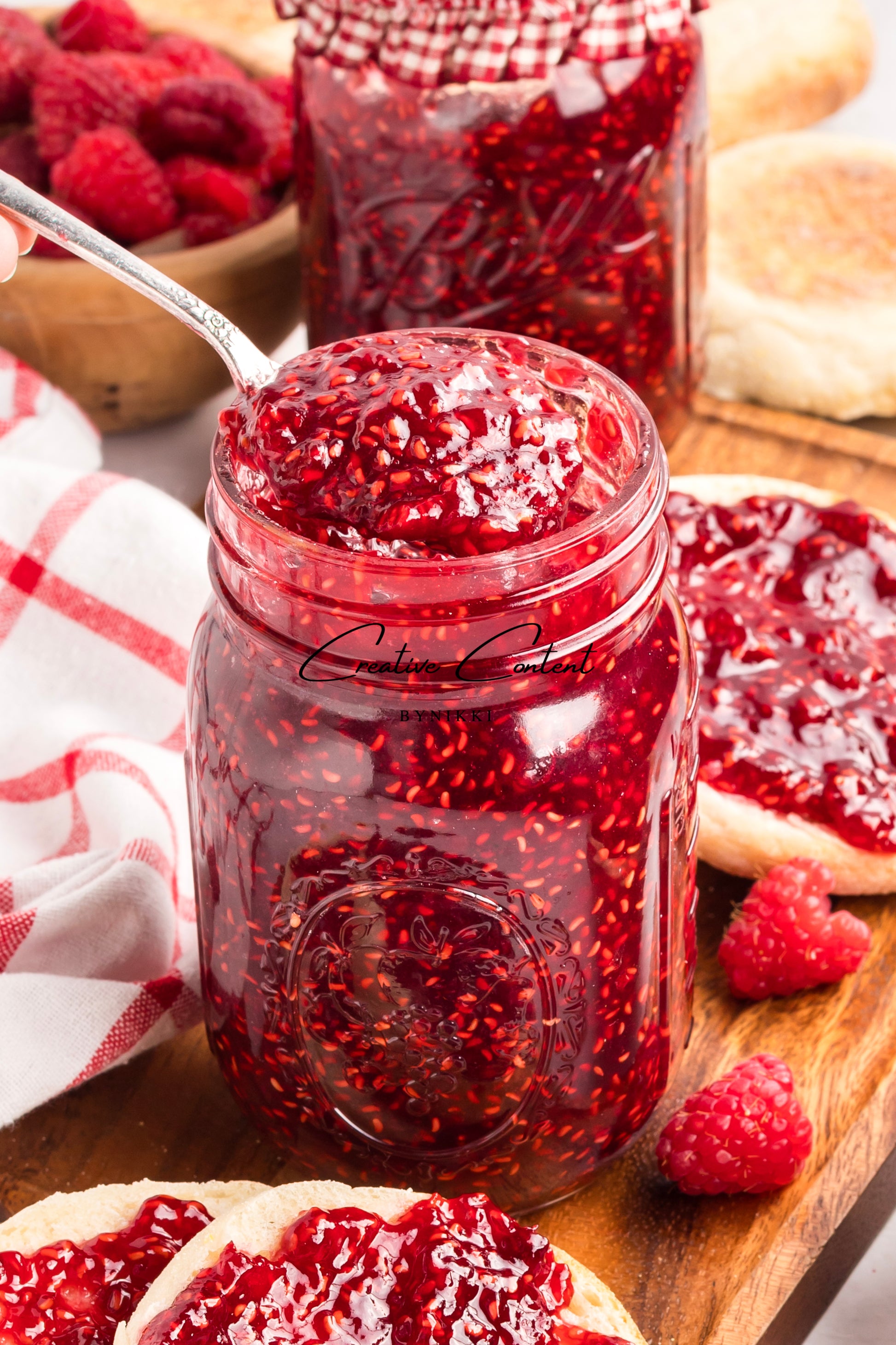 Jar of red raspberry jam on a wooden board with bread and raspberries.