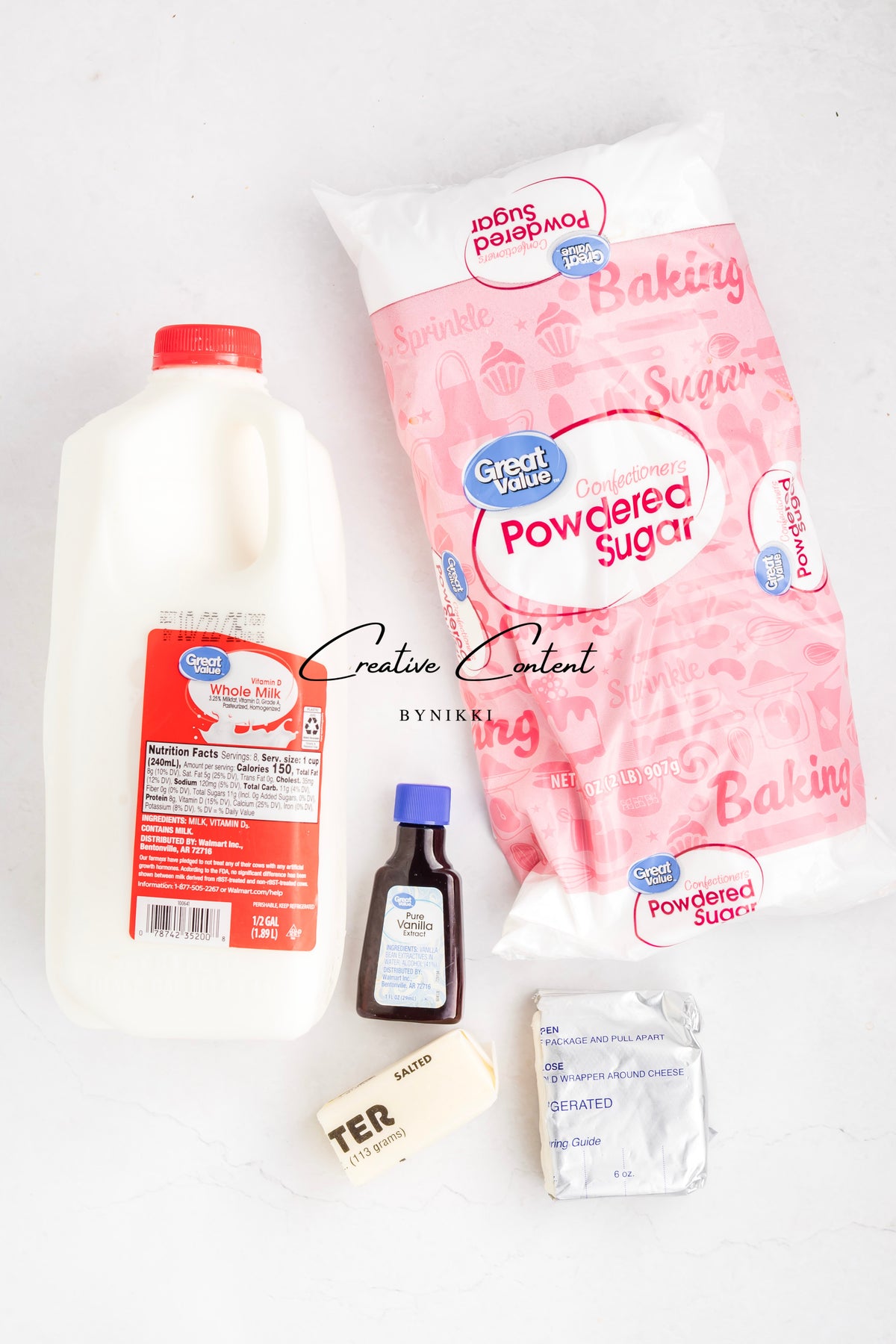 Ingredients for a Strawberry Crunch Cake - Exclusive, including a half-gallon of whole milk, powdered sugar, vanilla extract, a stick of salted butter, and a block of cream cheese arranged on a white surface.
