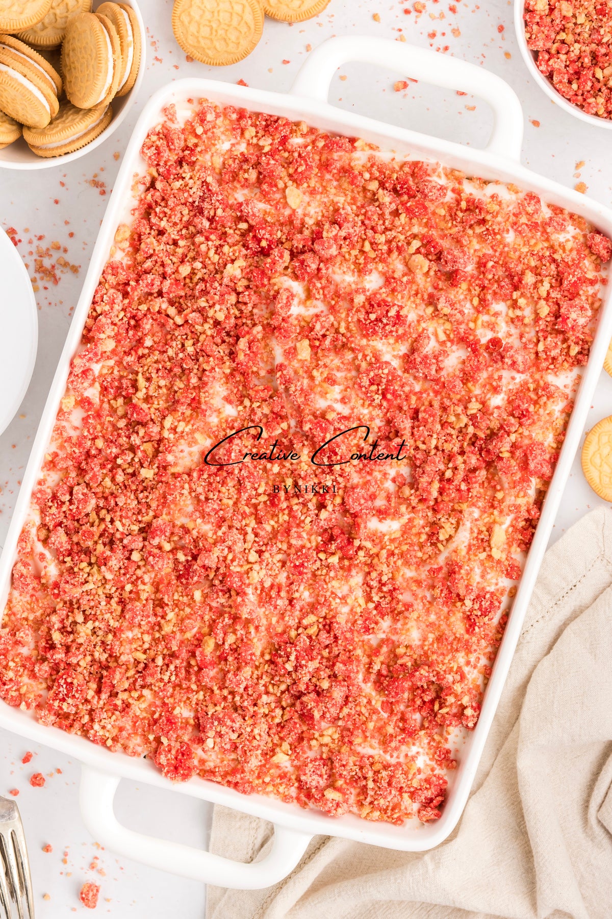 Rectangular Strawberry Crunch Cake - Exclusive in a white baking dish topped with red and golden cake crumbles, surrounded by sandwich cookies.