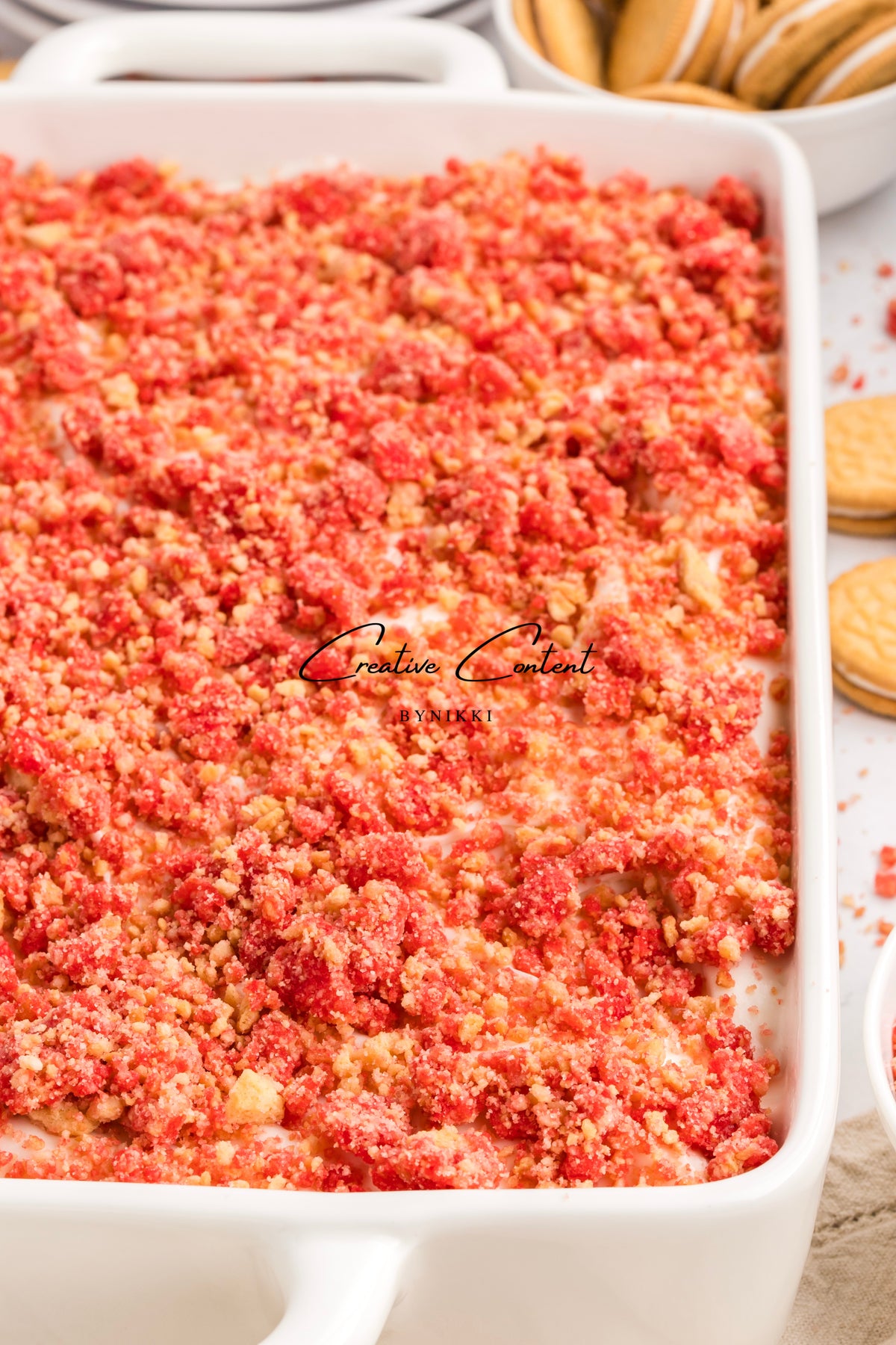 A rectangular baking dish filled with a Strawberry Crunch Cake - Exclusive, topped with a layer of red strawberry crumbles.