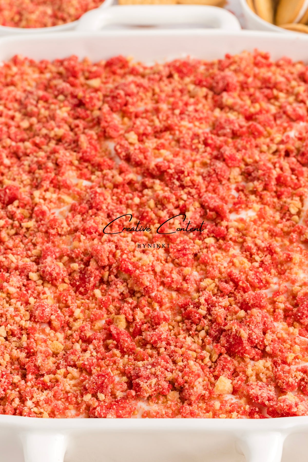 A white rectangular baking dish filled with a Strawberry Crunch Cake - Exclusive, topped with a layer of red and golden yellow crumbles.