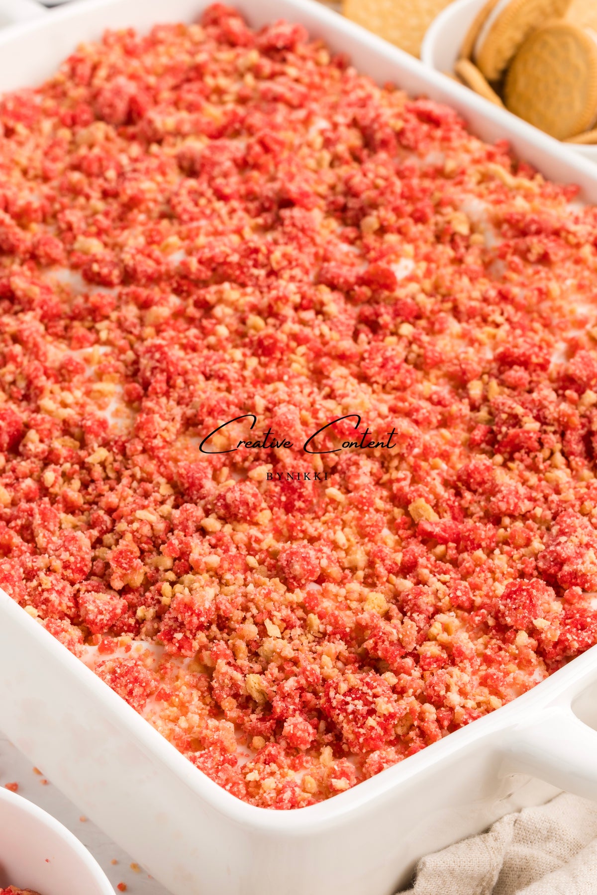 Rectangular white baking dish filled with a Strawberry Crunch Cake - Exclusive topped with red and tan cookie crumbles.