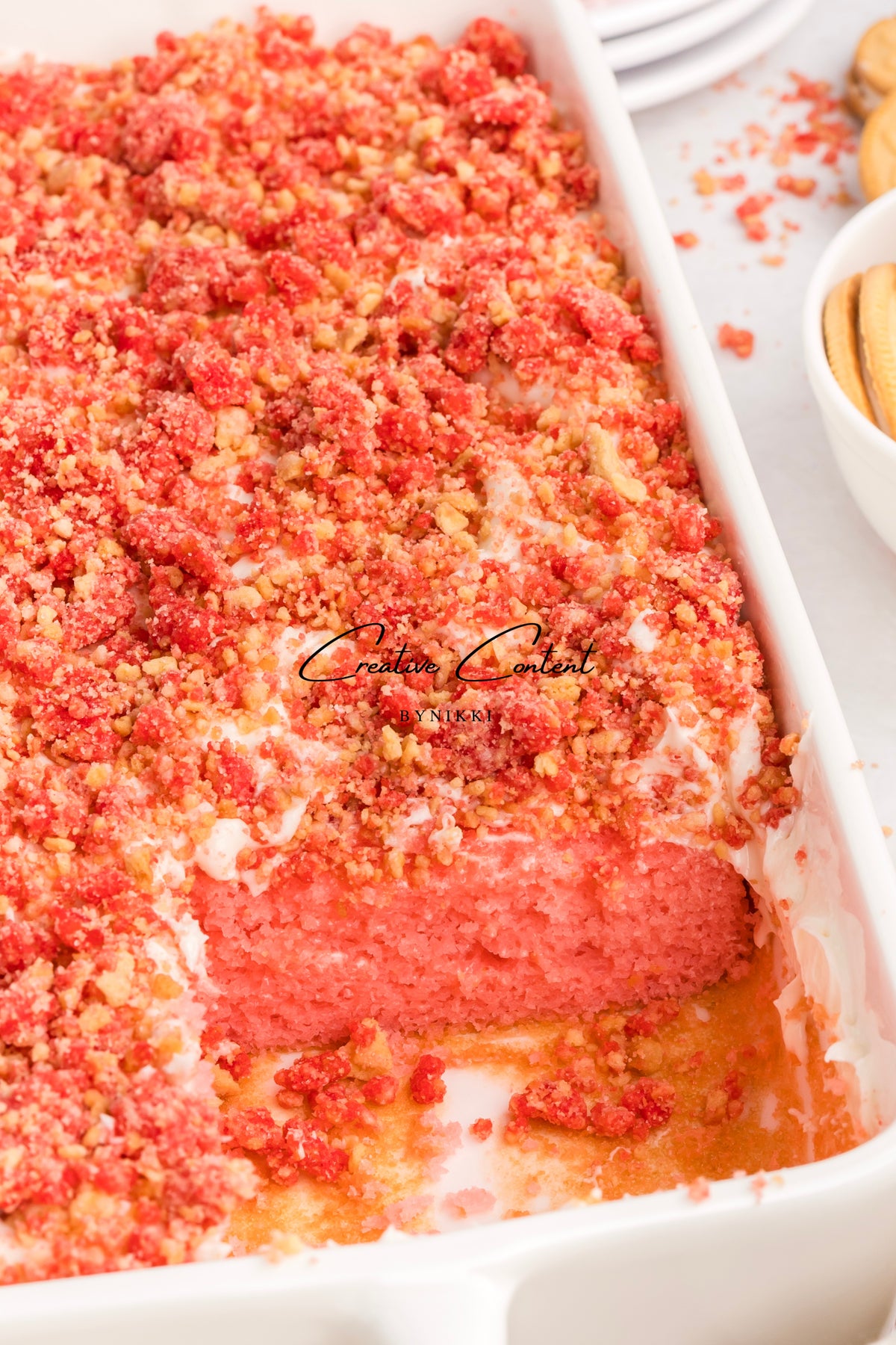A square pan of Strawberry Crunch Cake - Exclusive topped with a layer of red and tan crumbles, with one piece removed.