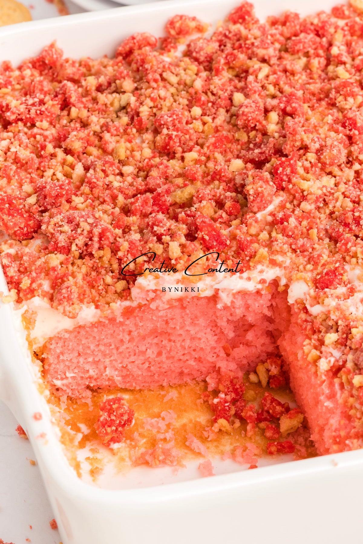 A Strawberry Crunch Cake - Exclusive in a white baking dish, topped with a pink, red, and crumbly strawberry-flavored streusel.
