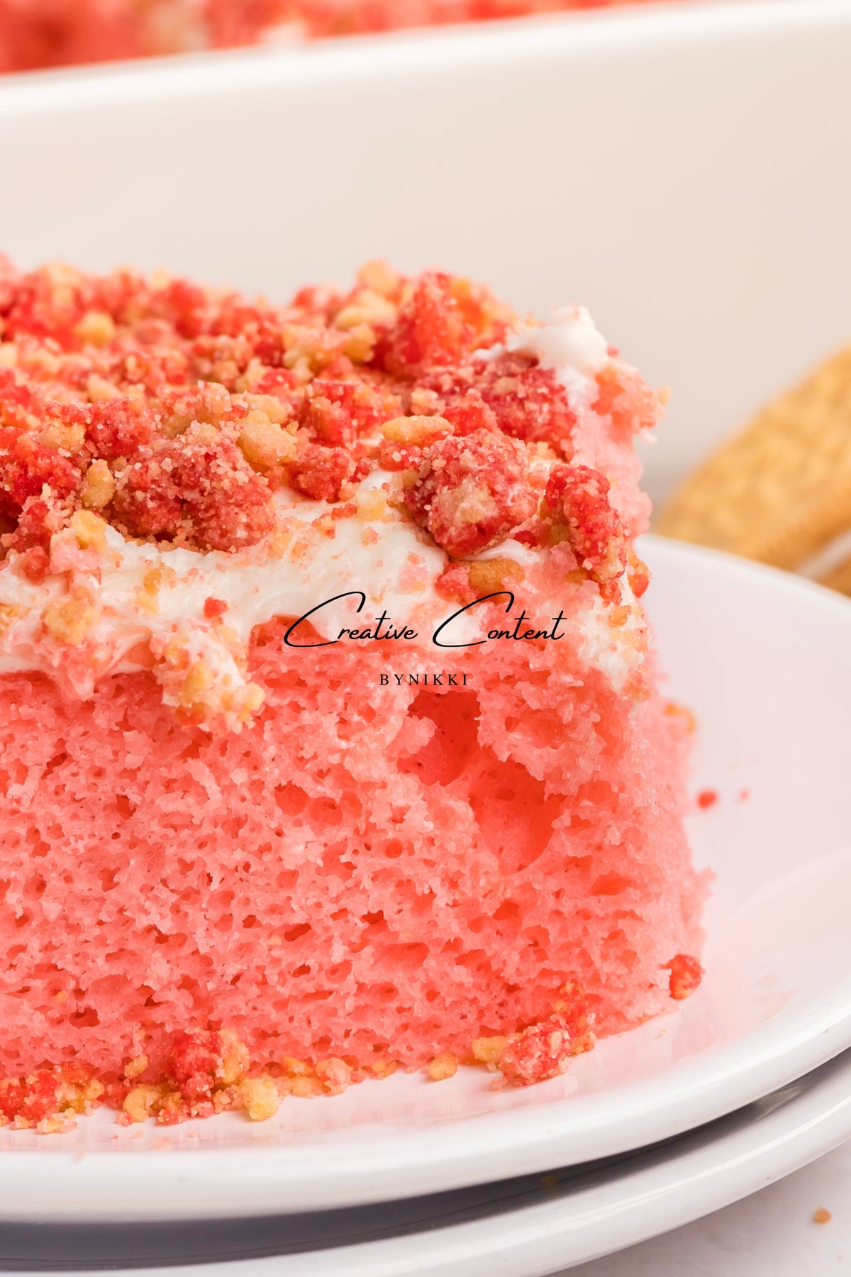A slice of Strawberry Crunch Cake - Exclusive with vanilla frosting and red cake crumbles on a white plate.
