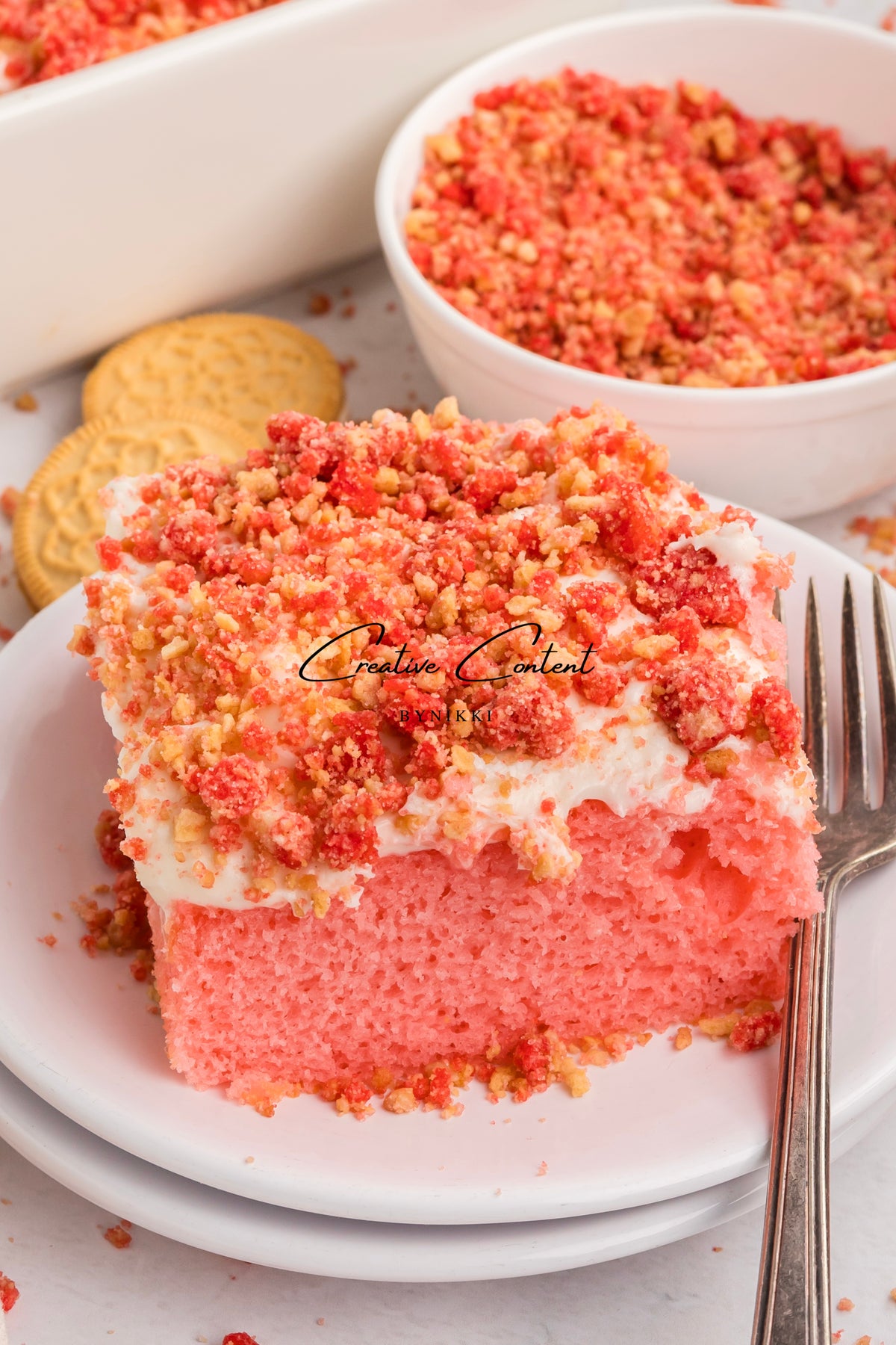 A slice of Strawberry Crunch Cake - Exclusive with vanilla frosting on a white plate with a fork.