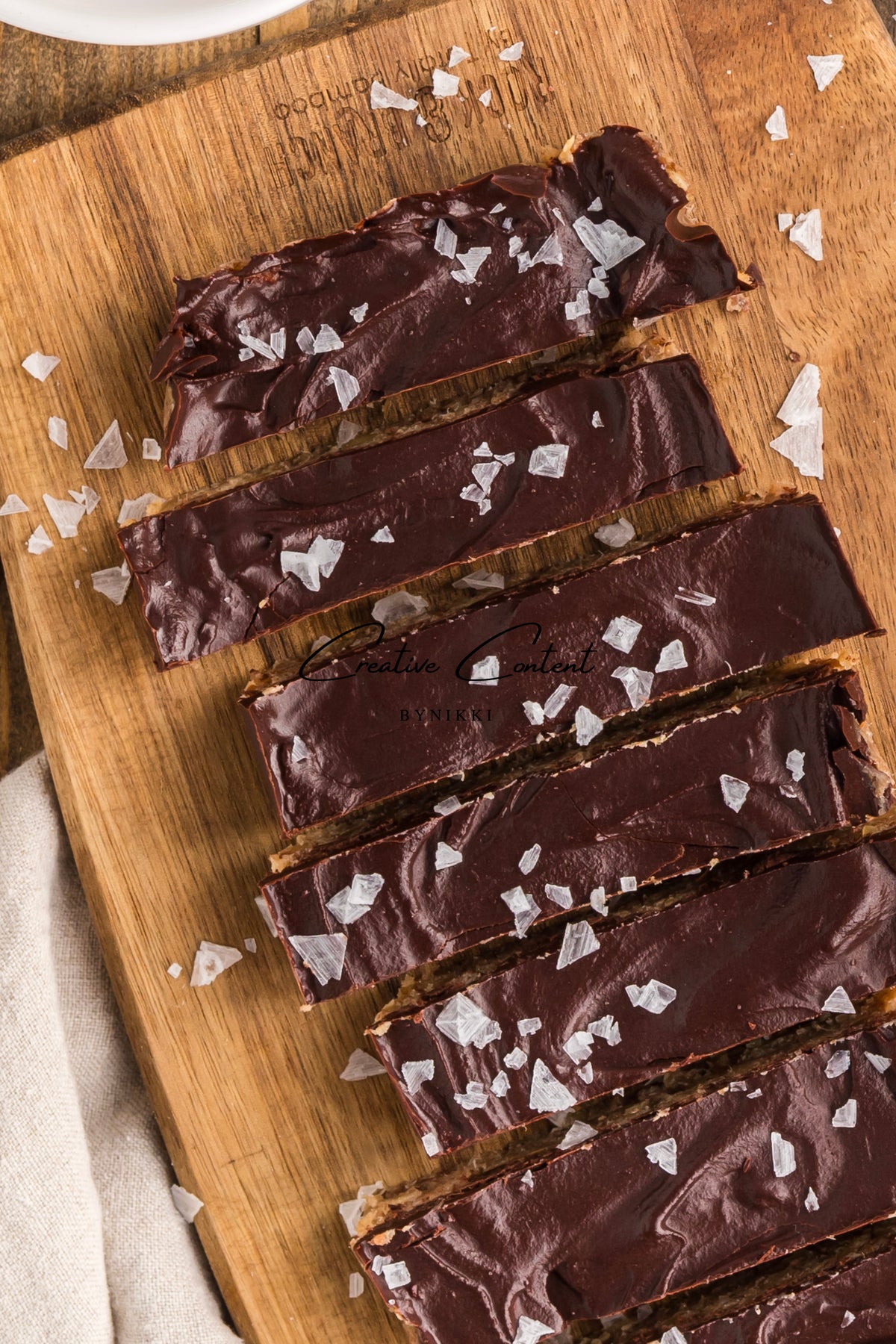 Five Walnut Date Bars - Exclusive coated in chocolate and topped with flaky sea salt, arranged on a wooden board.