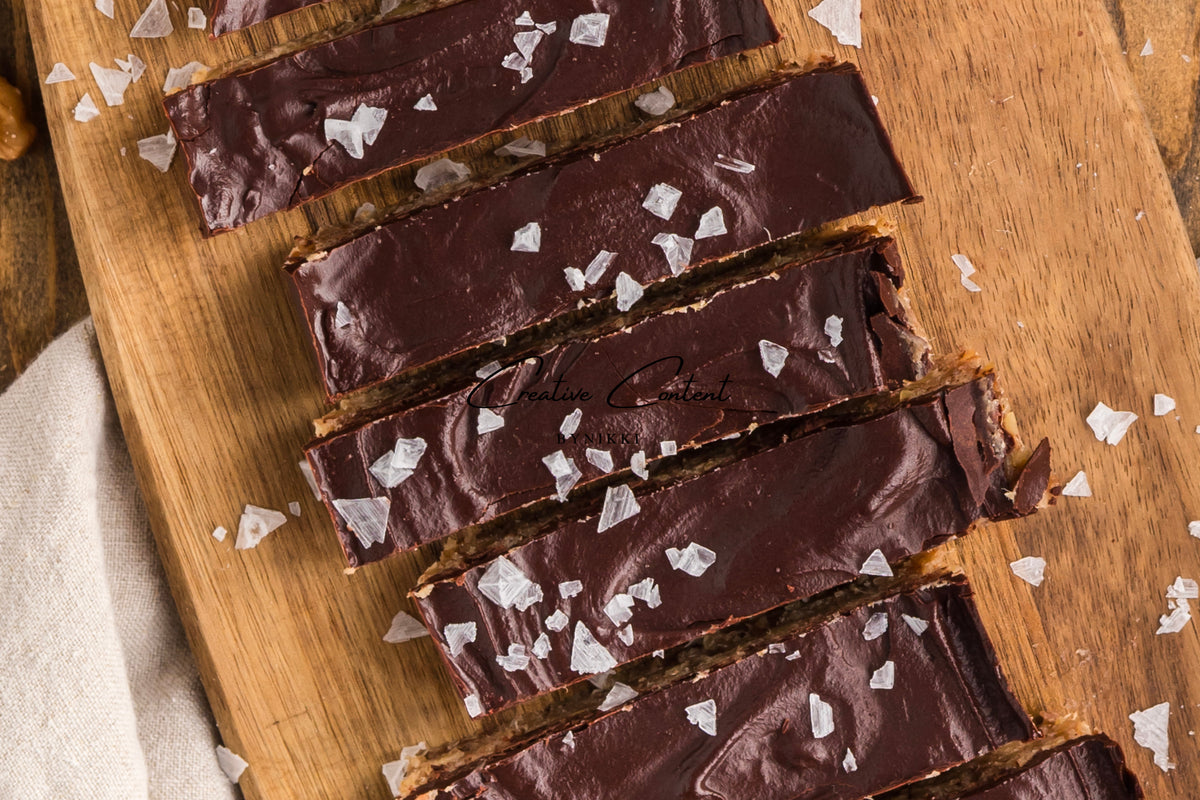 Walnut Date Bars - Exclusive chocolate-coated date bars sprinkled with sea salt, arranged on a wooden cutting board.