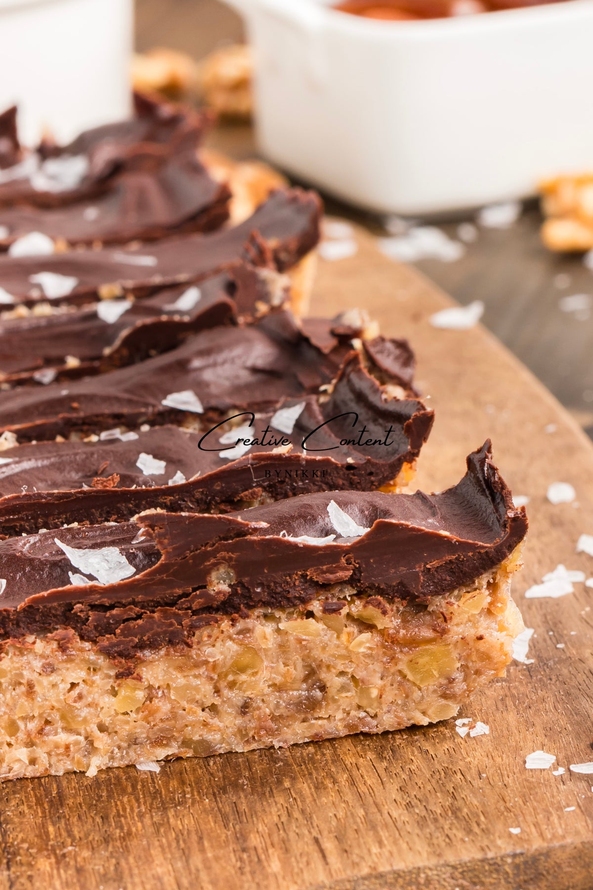 Exclusive Walnut Date Bars, rectangular and topped with dark chocolate and sea salt, arranged on a wooden board.