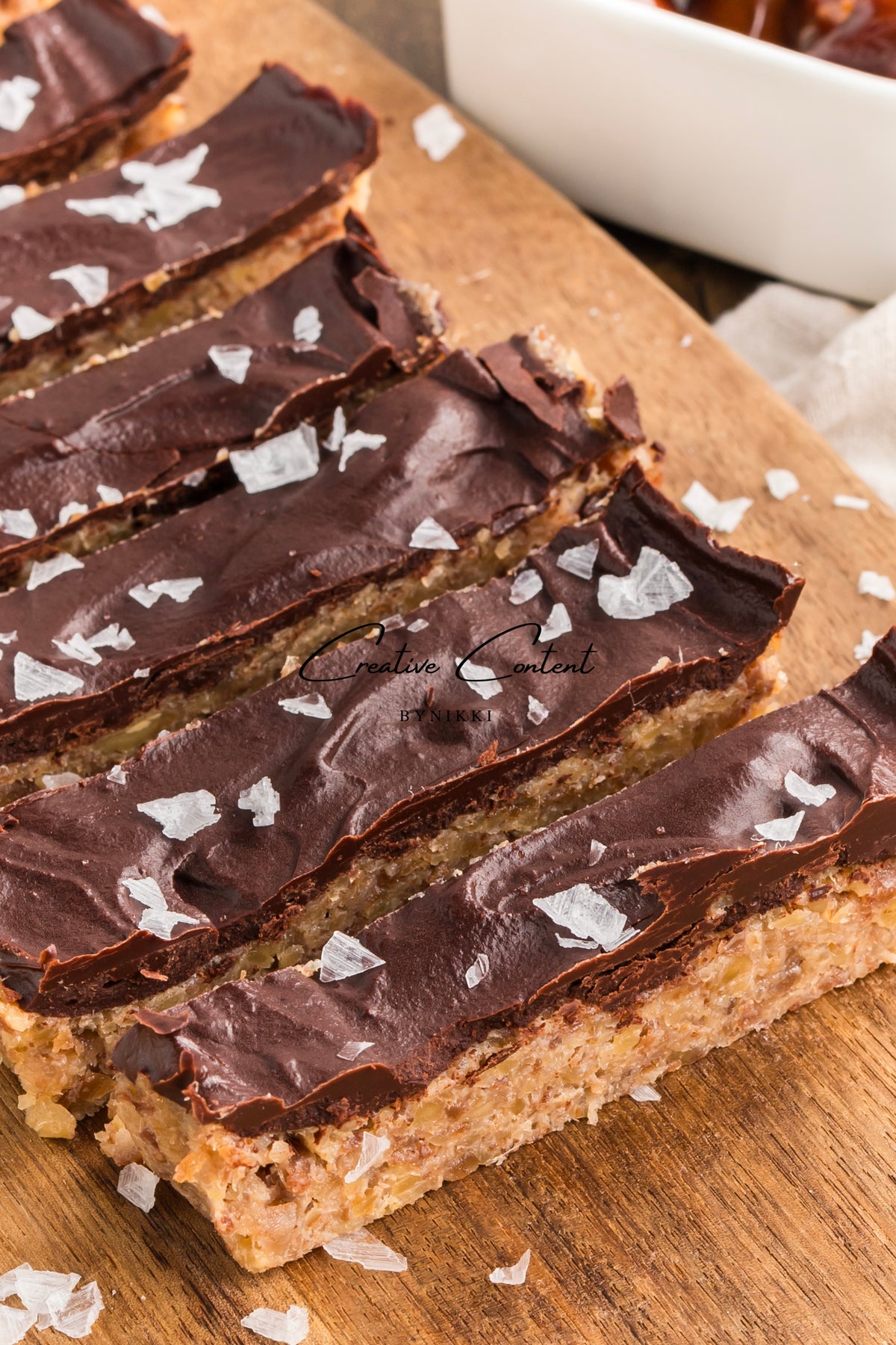 Rectangular Walnut Date Bars - Exclusive topped with chocolate ganache and sea salt flakes, arranged on a wooden board.