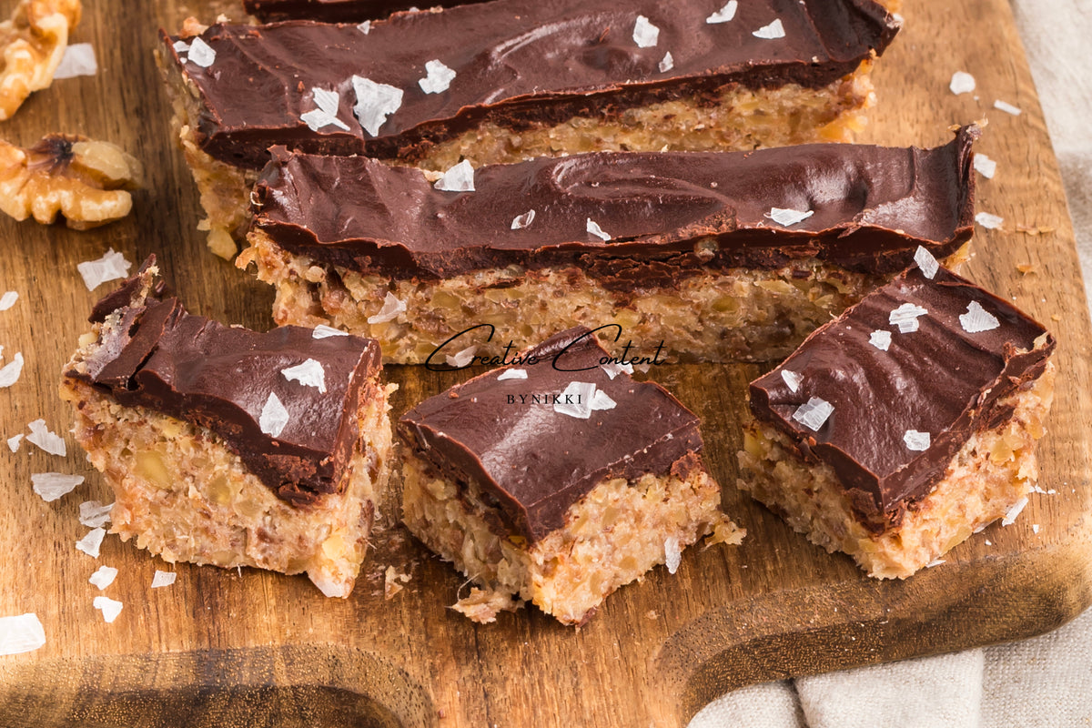 Rectangular Walnut Date Bars - Exclusive topped with dark chocolate and sea salt flakes on a wooden cutting board.