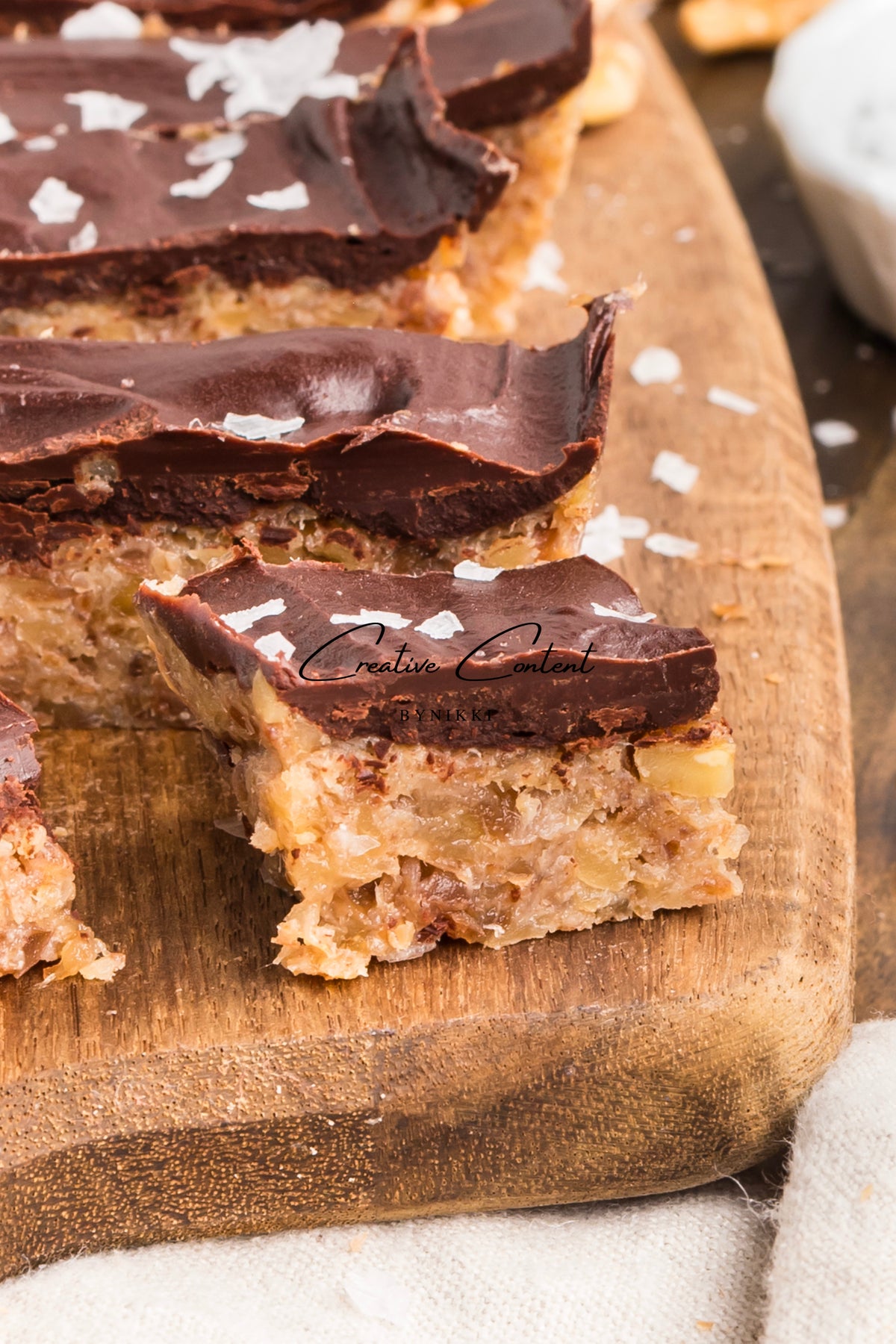 Rectangular, naturally sweetened Walnut Date Bars - Exclusive topped with chocolate ganache and sea salt on a wooden board.