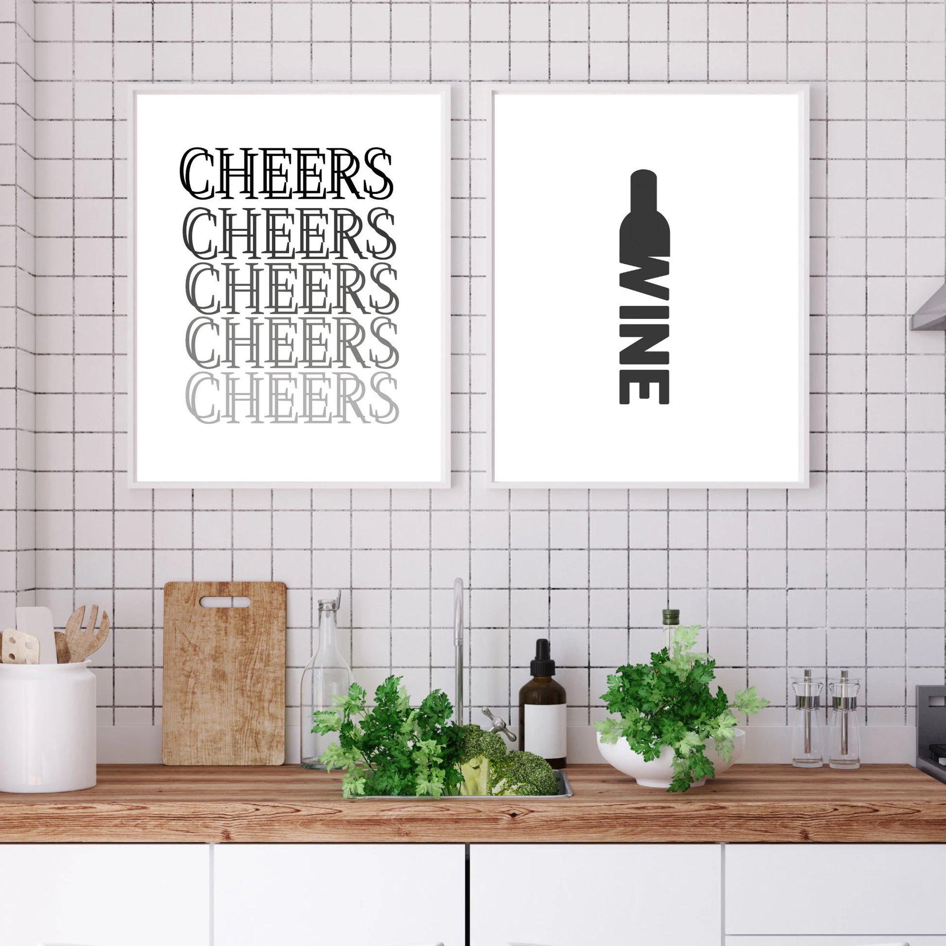 Two framed prints on a tiled wall above a kitchen counter with plants and bottles.